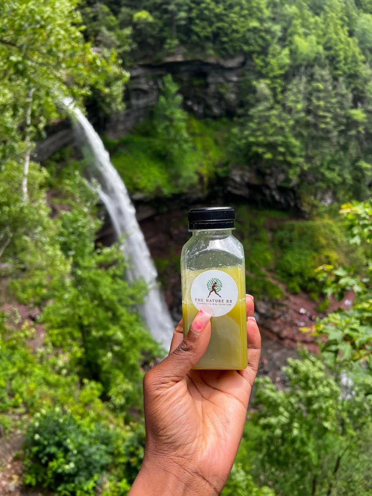 A hand holding a bottle labeled 'The Nature RX' with greenery and a waterfall in the background.