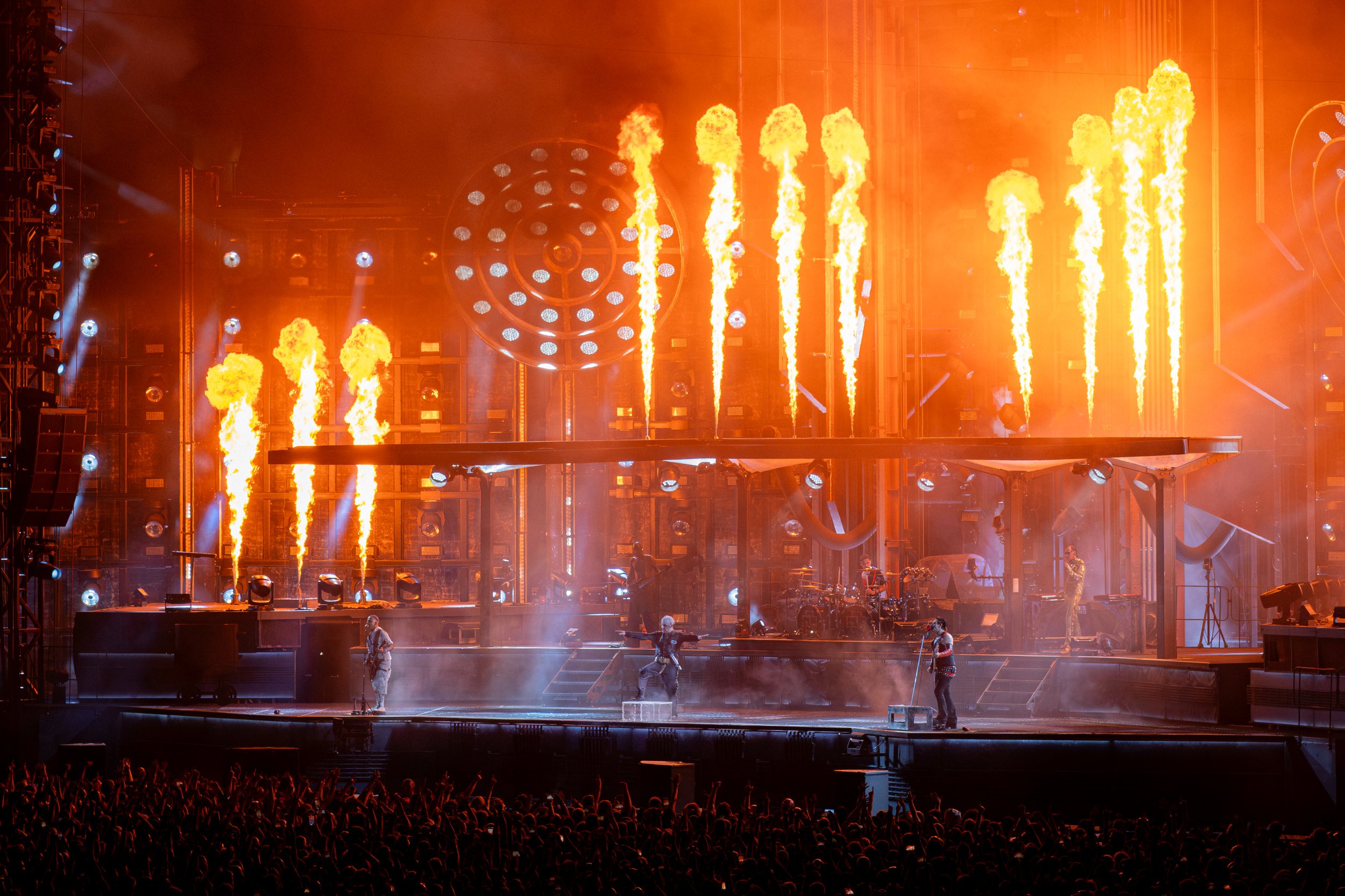 A concert stage with fire effects, musicians performing, and crowd in the foreground.