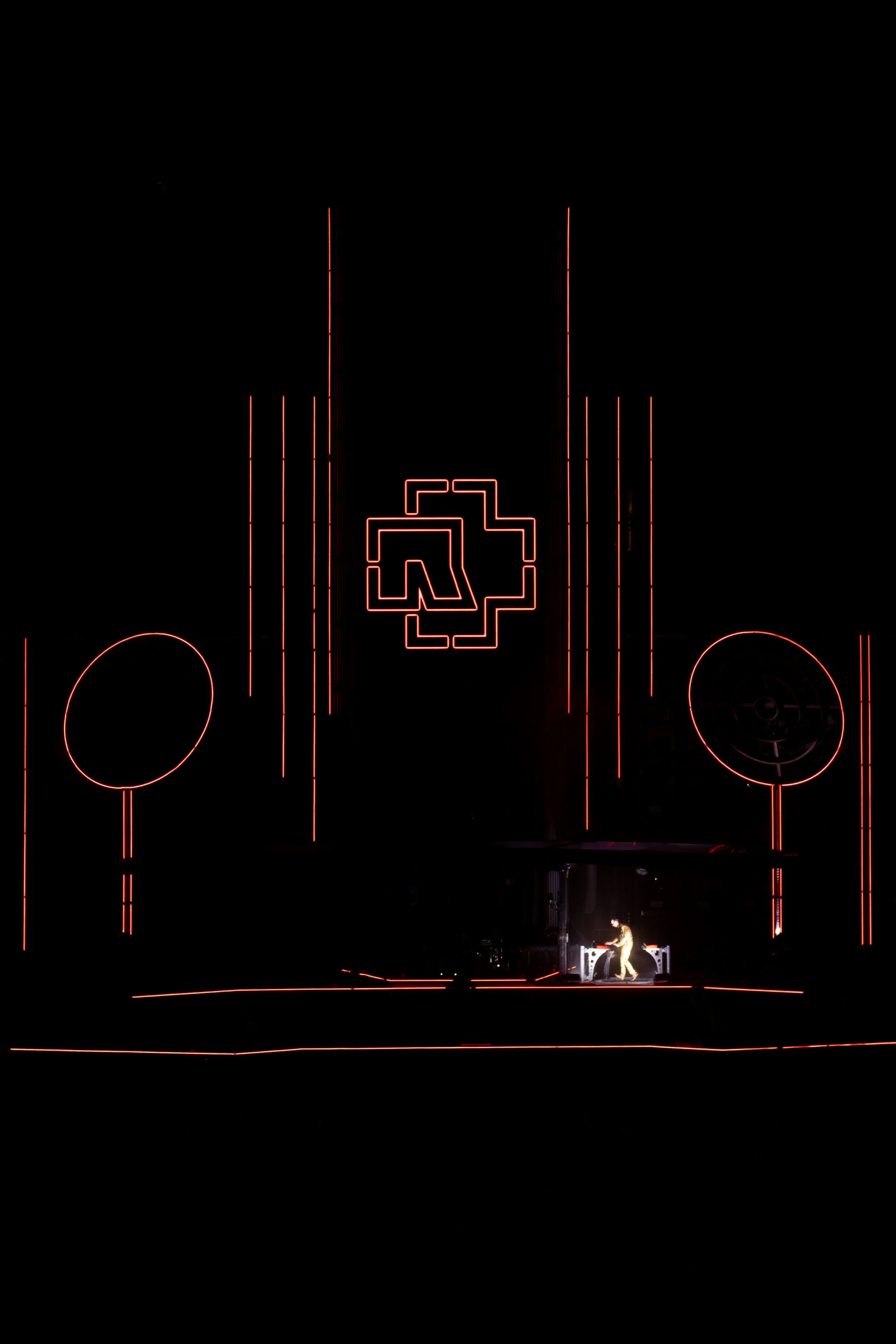 A performer on stage with a glowing red geometric background and a large logo in the center, as seen in a dark setting.