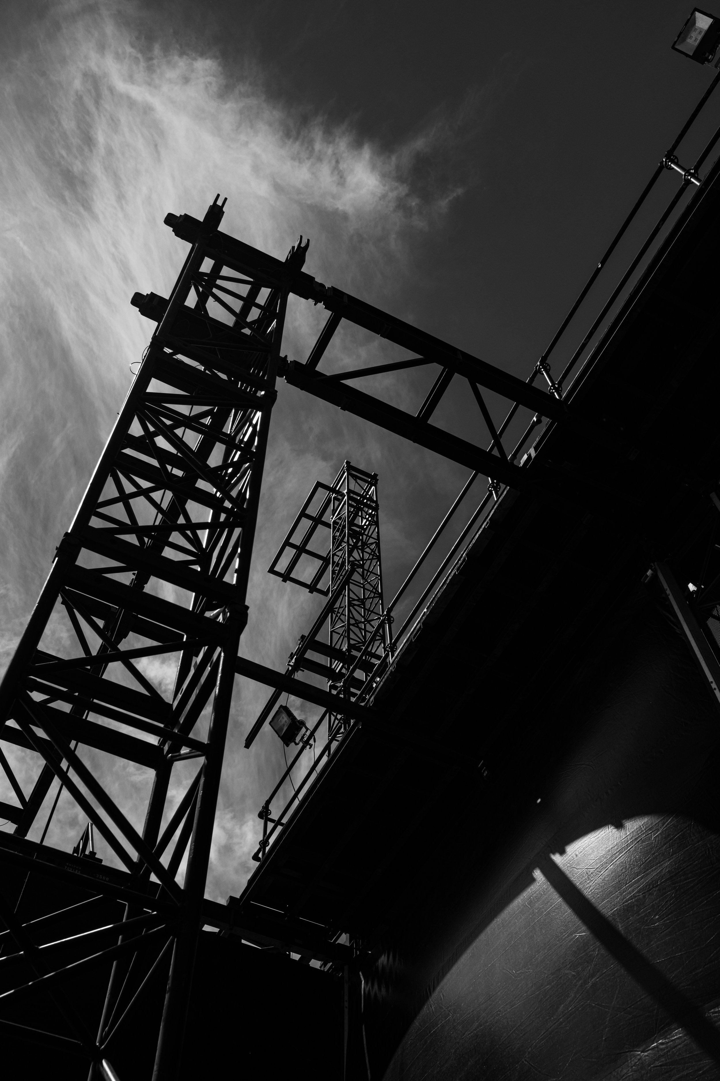 Silhouette of a tall construction crane against a cloudy sky in black and white.