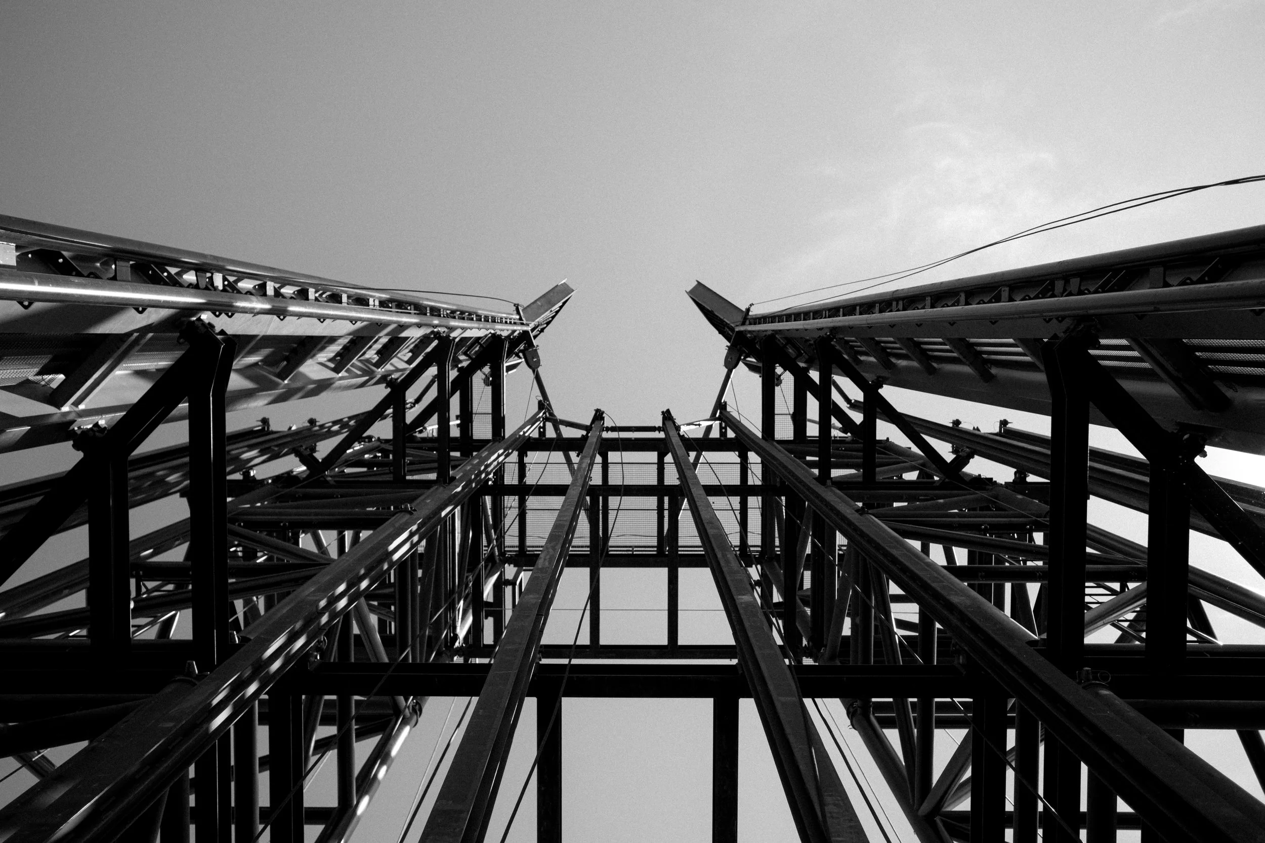 A black and white photo of a tall metal structure, taken from the ground looking straight up, with wires against the sky.