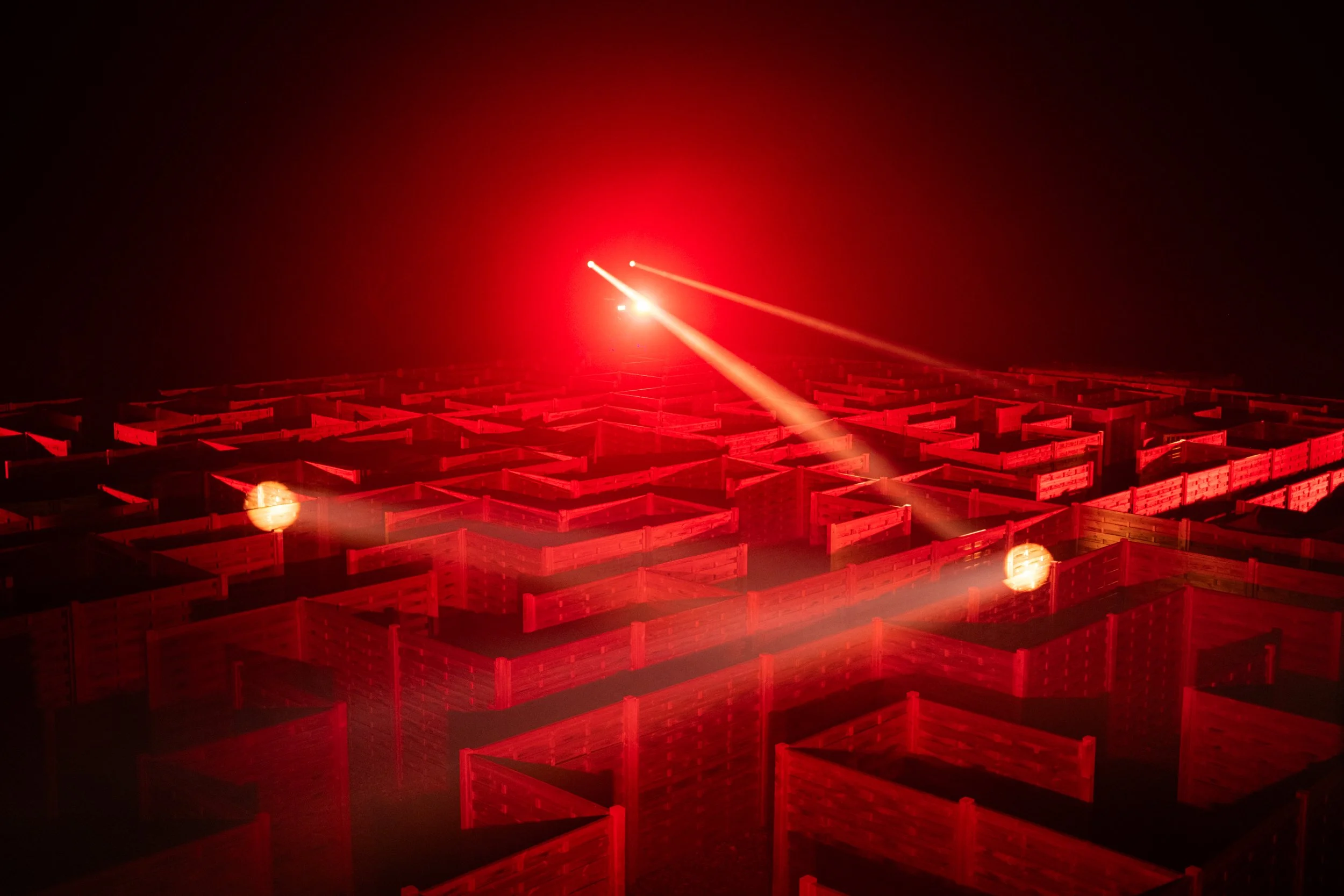 A large outdoor maze illuminated by red laser lights at night.