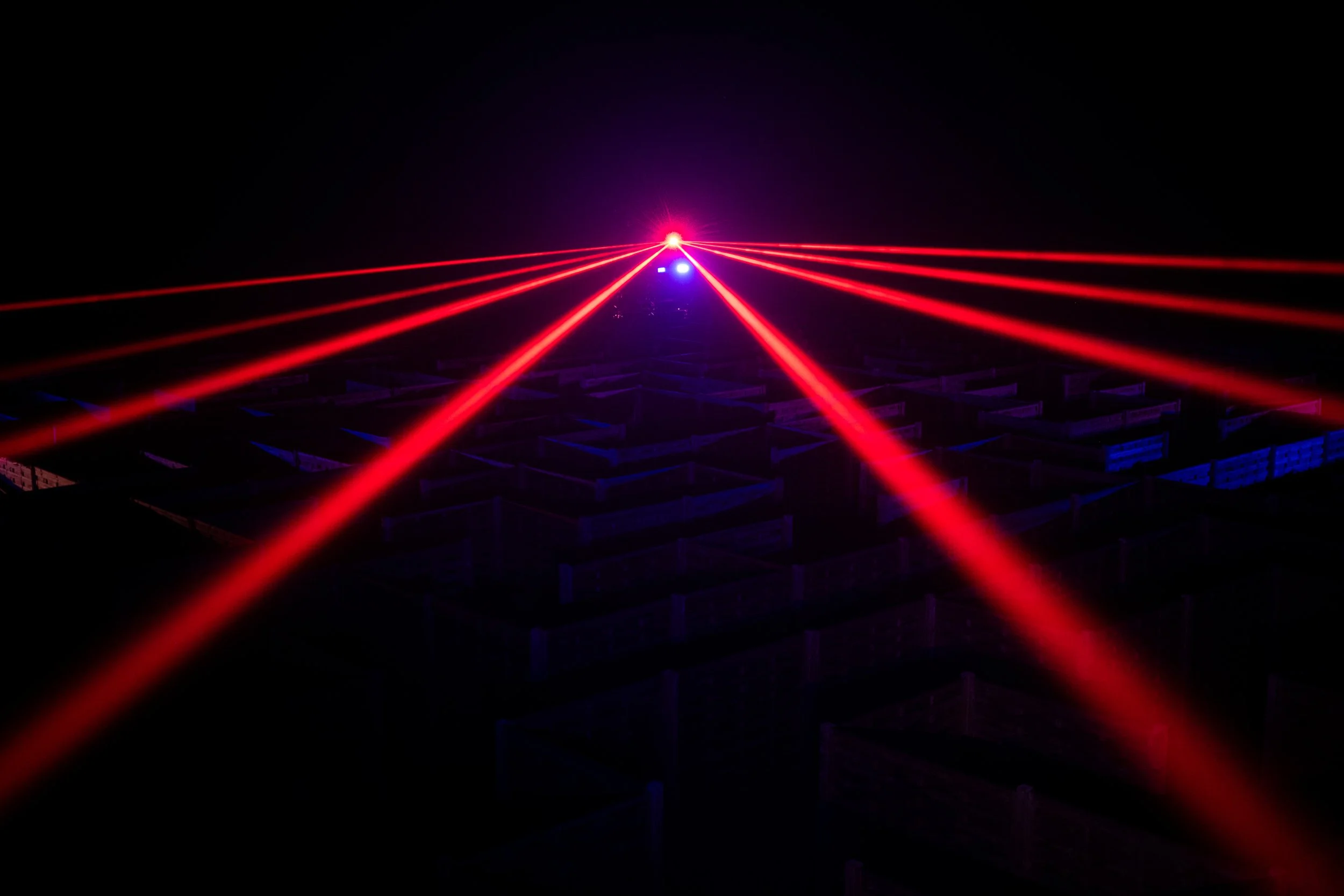 Laser light show with red and purple laser beams crossing over a dark background.