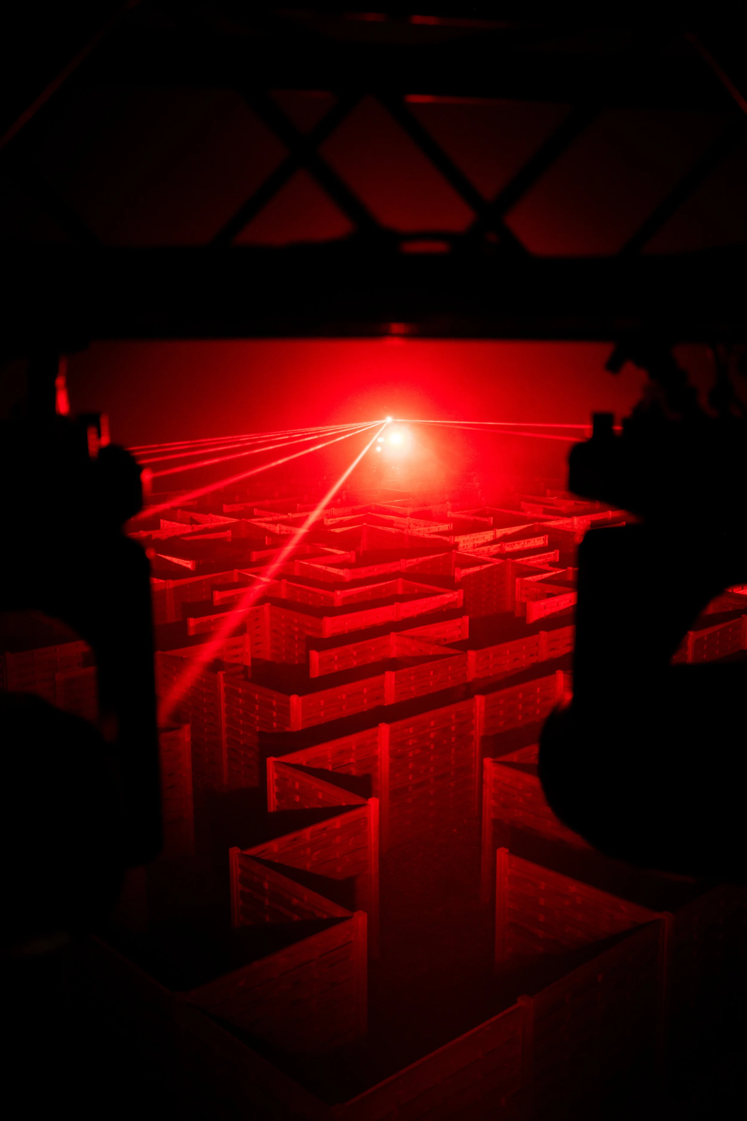 Red laser beams crossing over a three-dimensional grid of wooden crates in a dark environment.