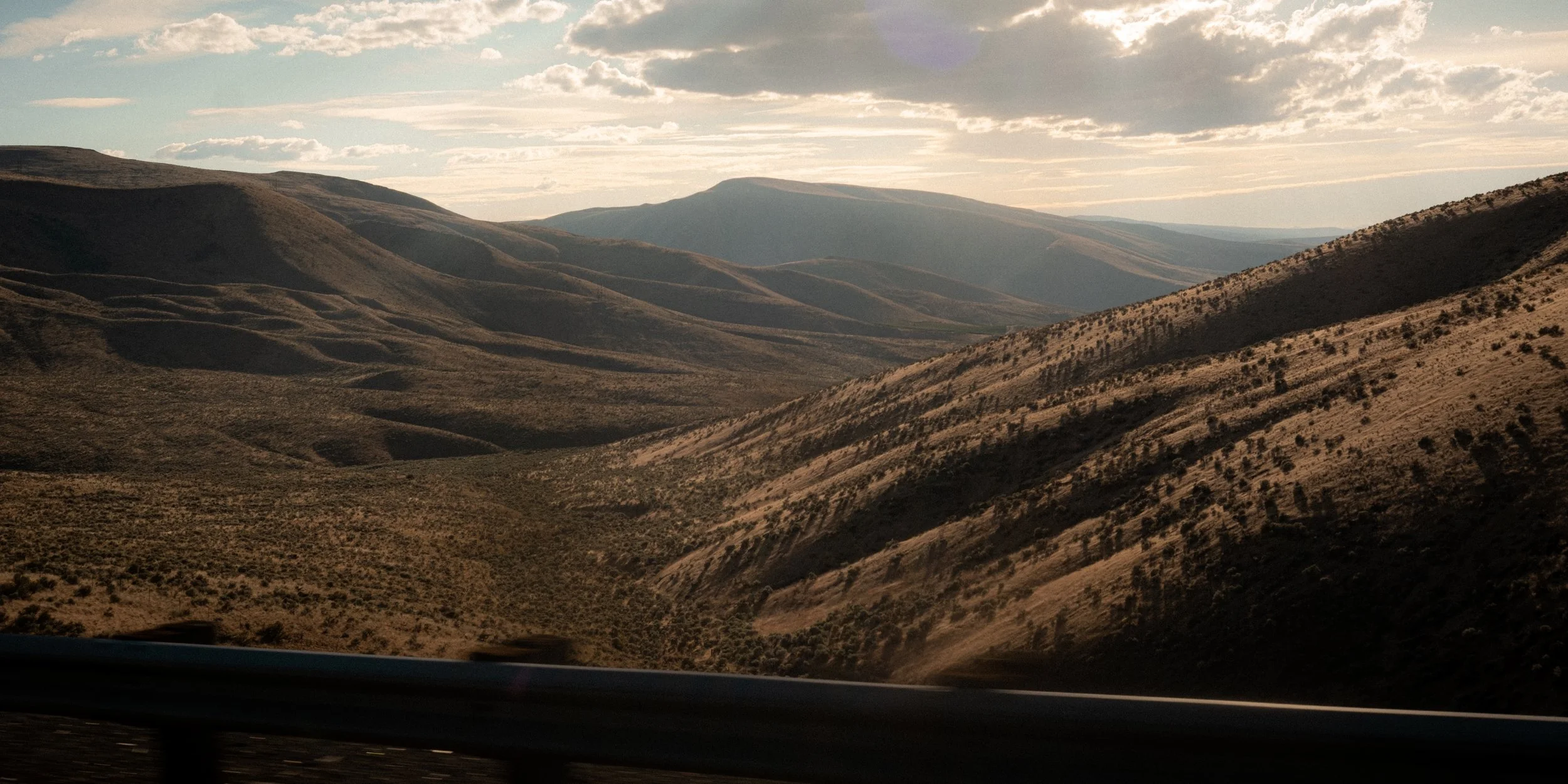 Hilly desert landscape with rolling brown hills, sparse vegetation, and a partly cloudy sky in Oregon.