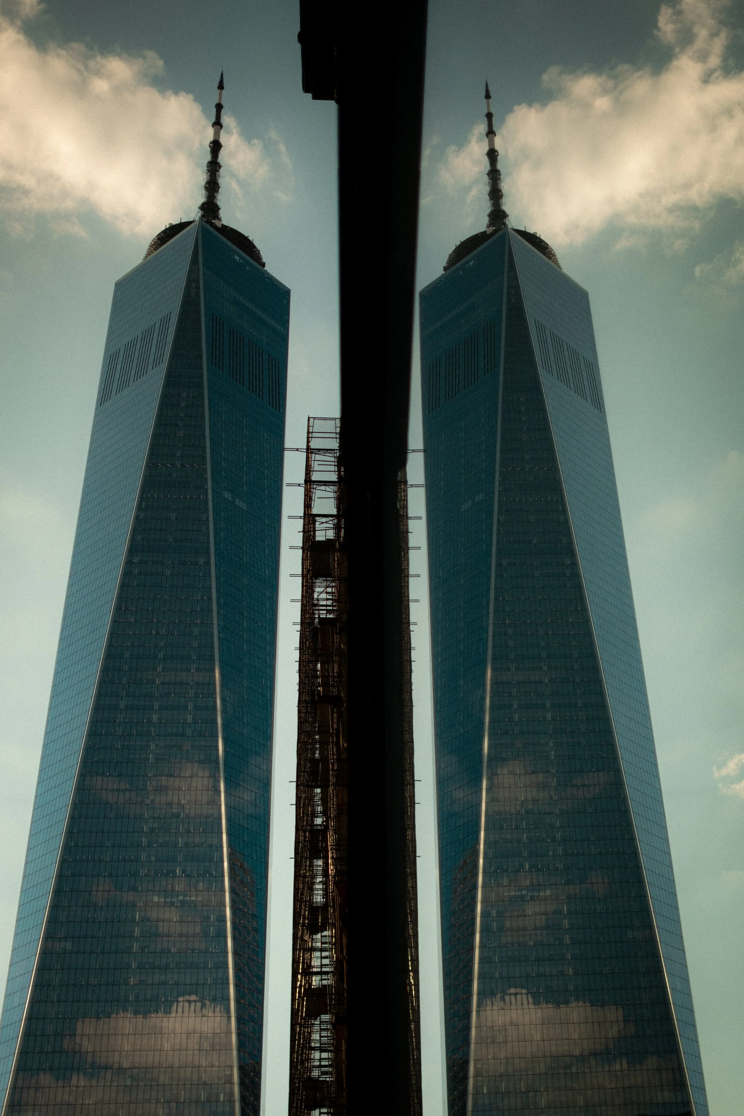 Looking up at the Twin Towers skyscrapers in New York City, reflected in a glass wall with a construction crane between the buildings.