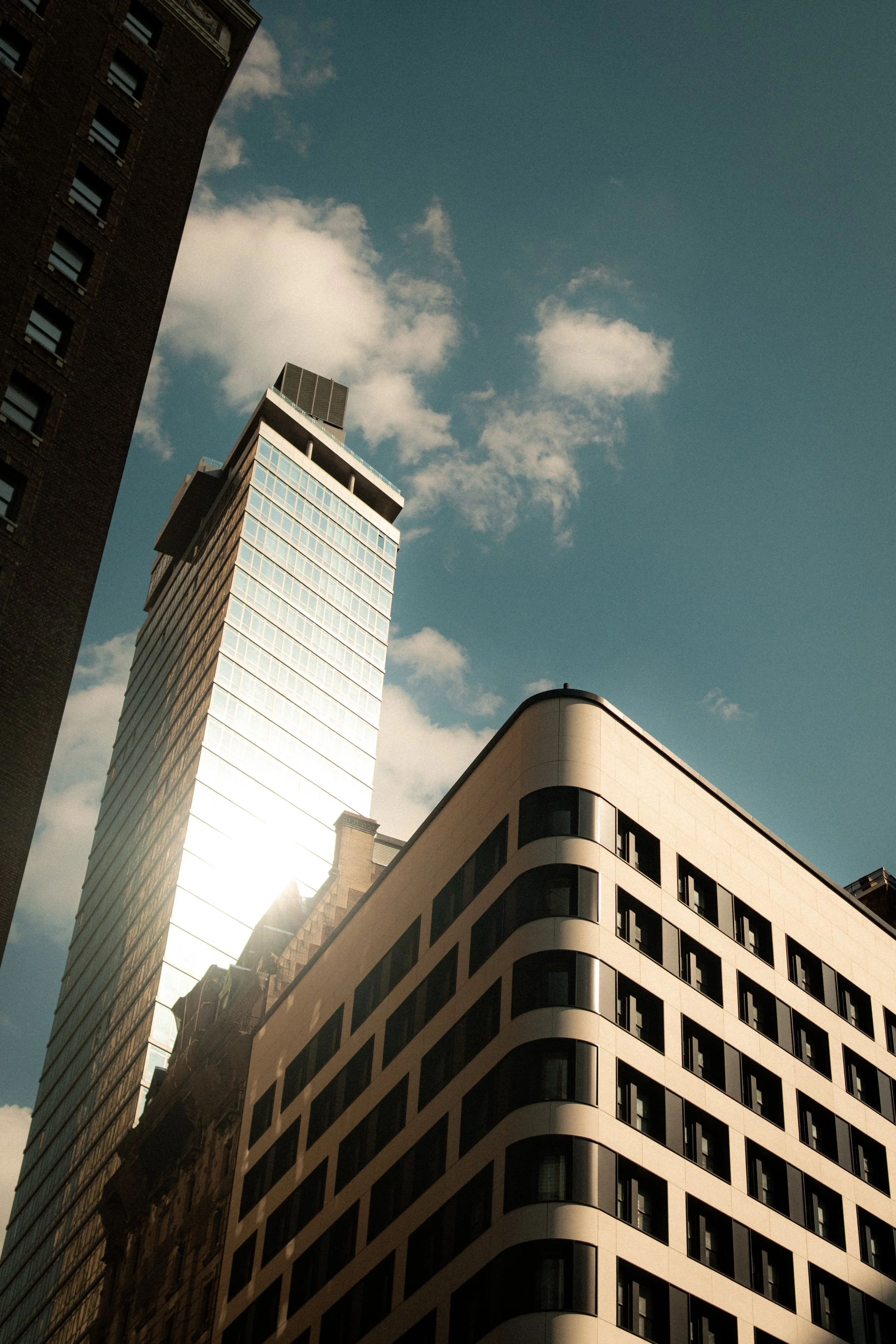 Several modern skyscrapers and buildings in New York City, with blue sky and clouds in the background.