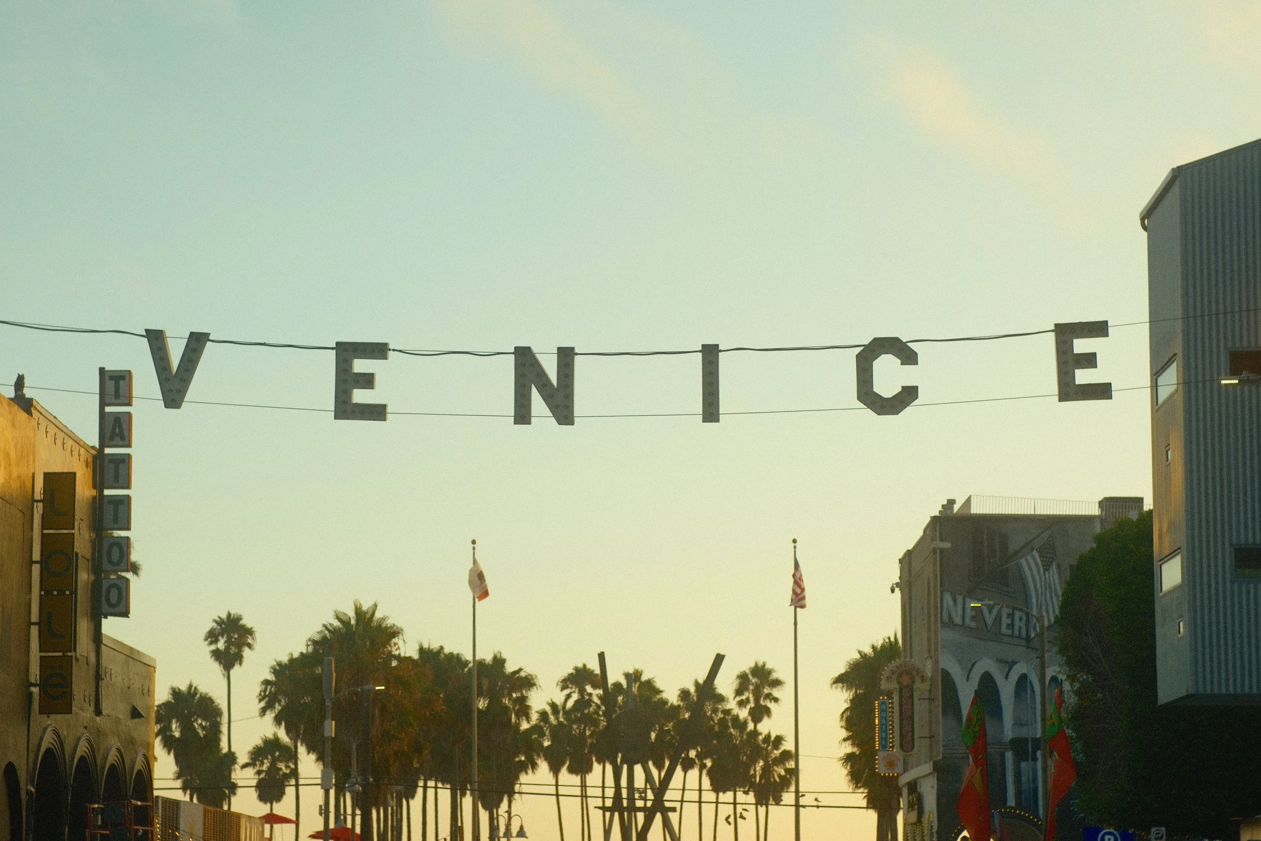 Street scene with buildings, palm trees, flags, and a decorative sign hanging across the street spelling 'VINTAGE' during sunset or early evening.