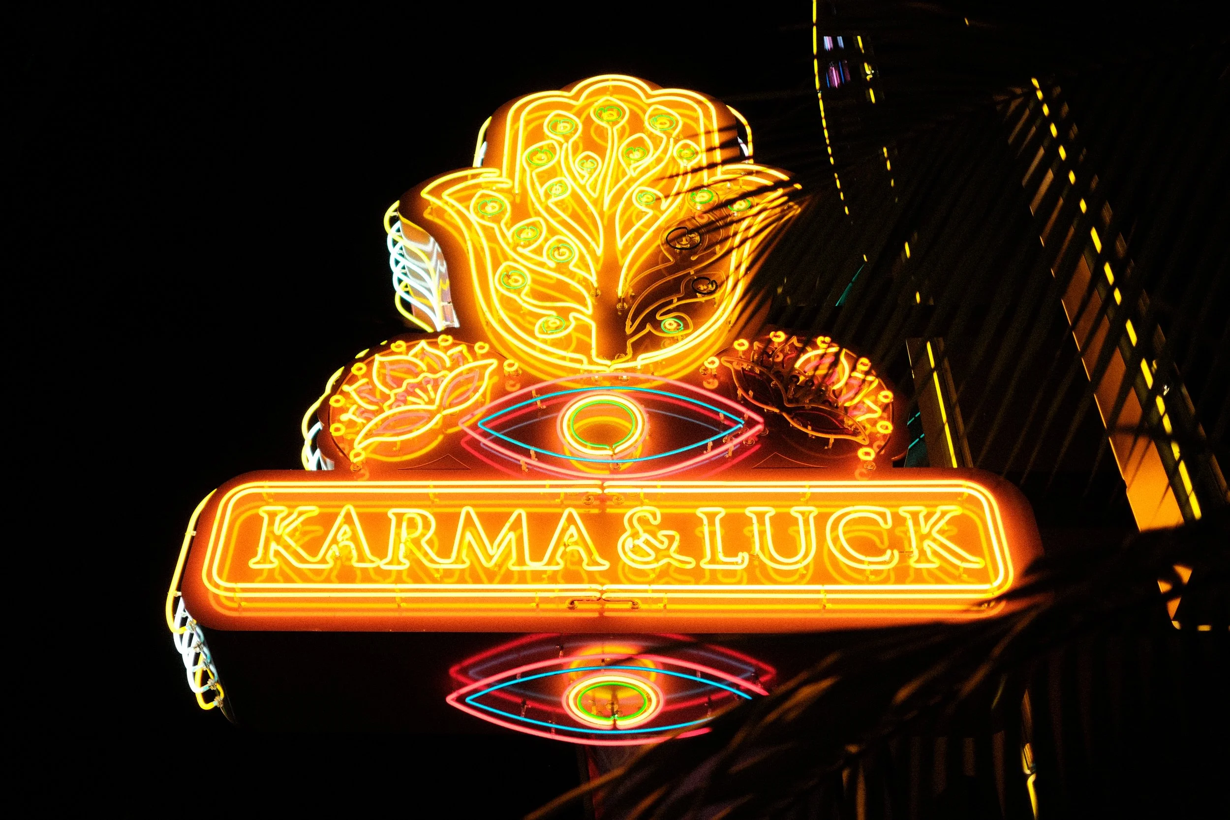 Neon sign with a lotus flower at the top and the words 'Karma & Luck' below, against a dark background.
