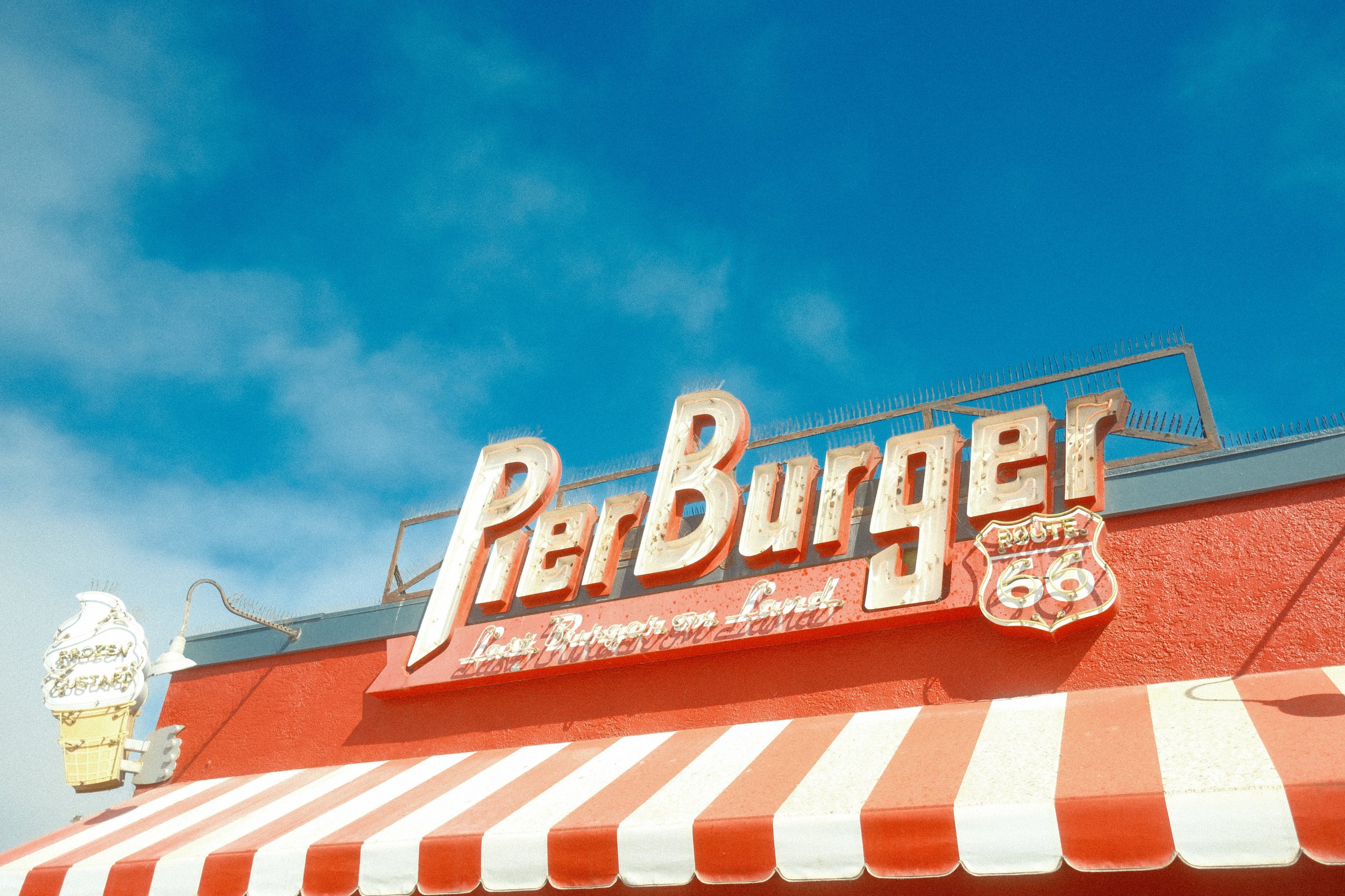 Vintage Route 66 sign on a red building with a red and white striped awning and outdoor lanterns, against a blue sky.