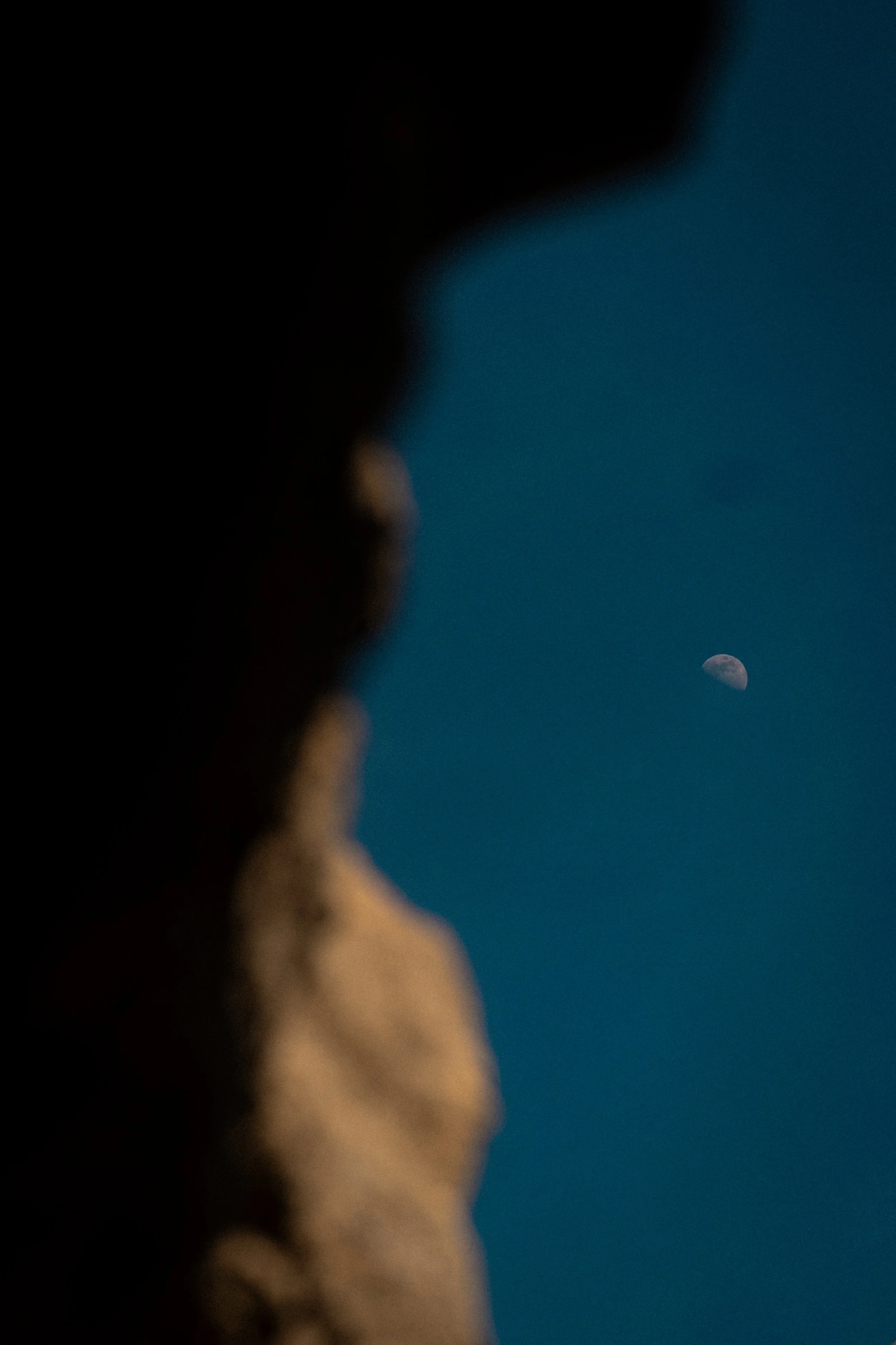 A blurred silhouette of a person looking at the moon in the night sky.