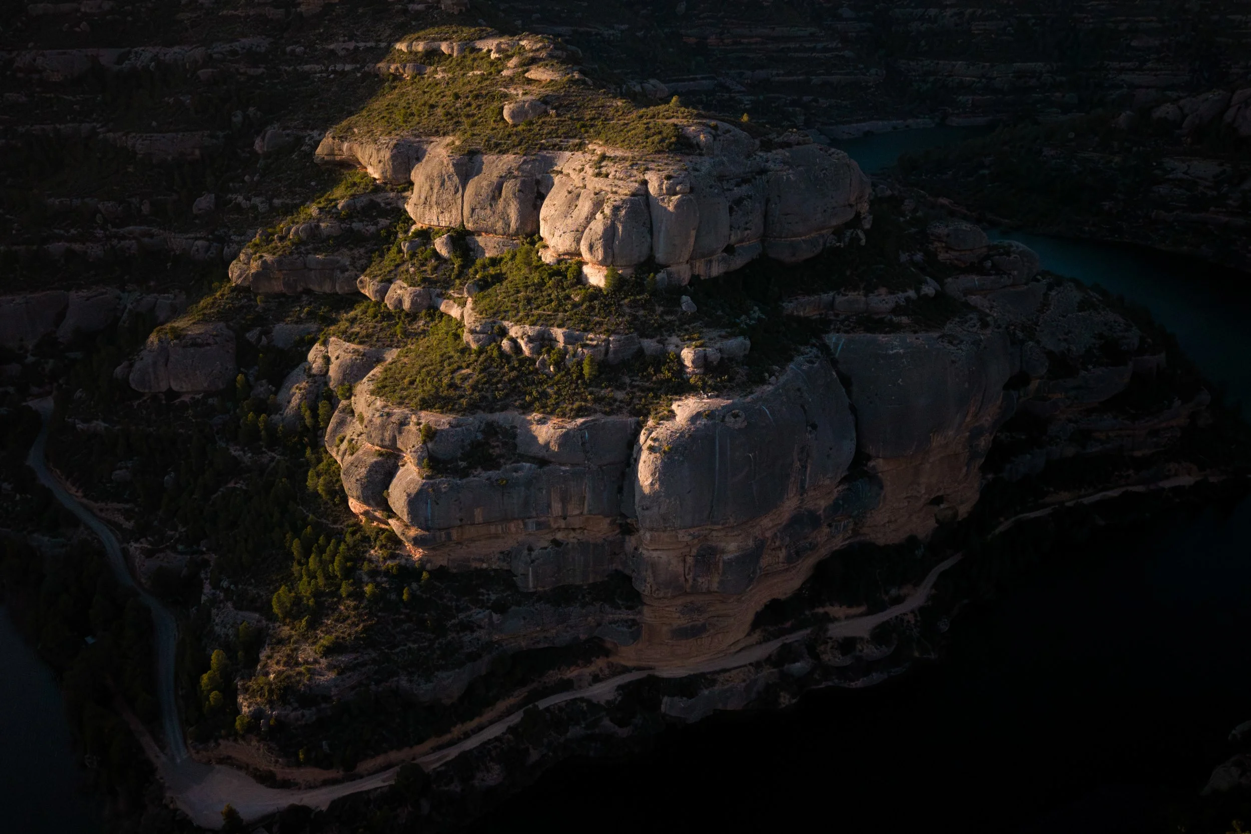 Aerial view of a massive rocky hill with steep sides, surrounded by winding roads and dense greenery.
