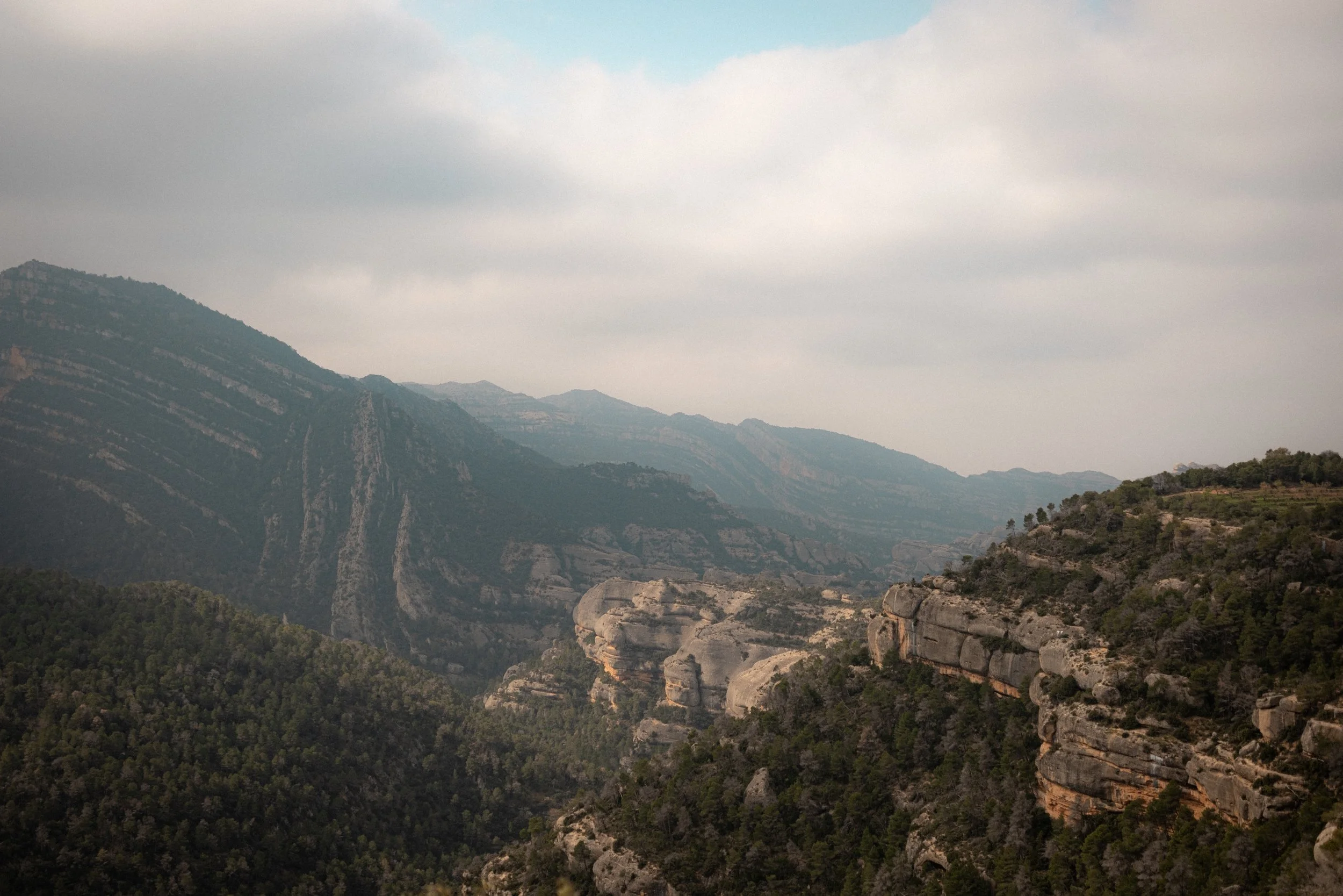 Mountain landscape with rugged cliffs, steep slopes, and a cloudy sky.