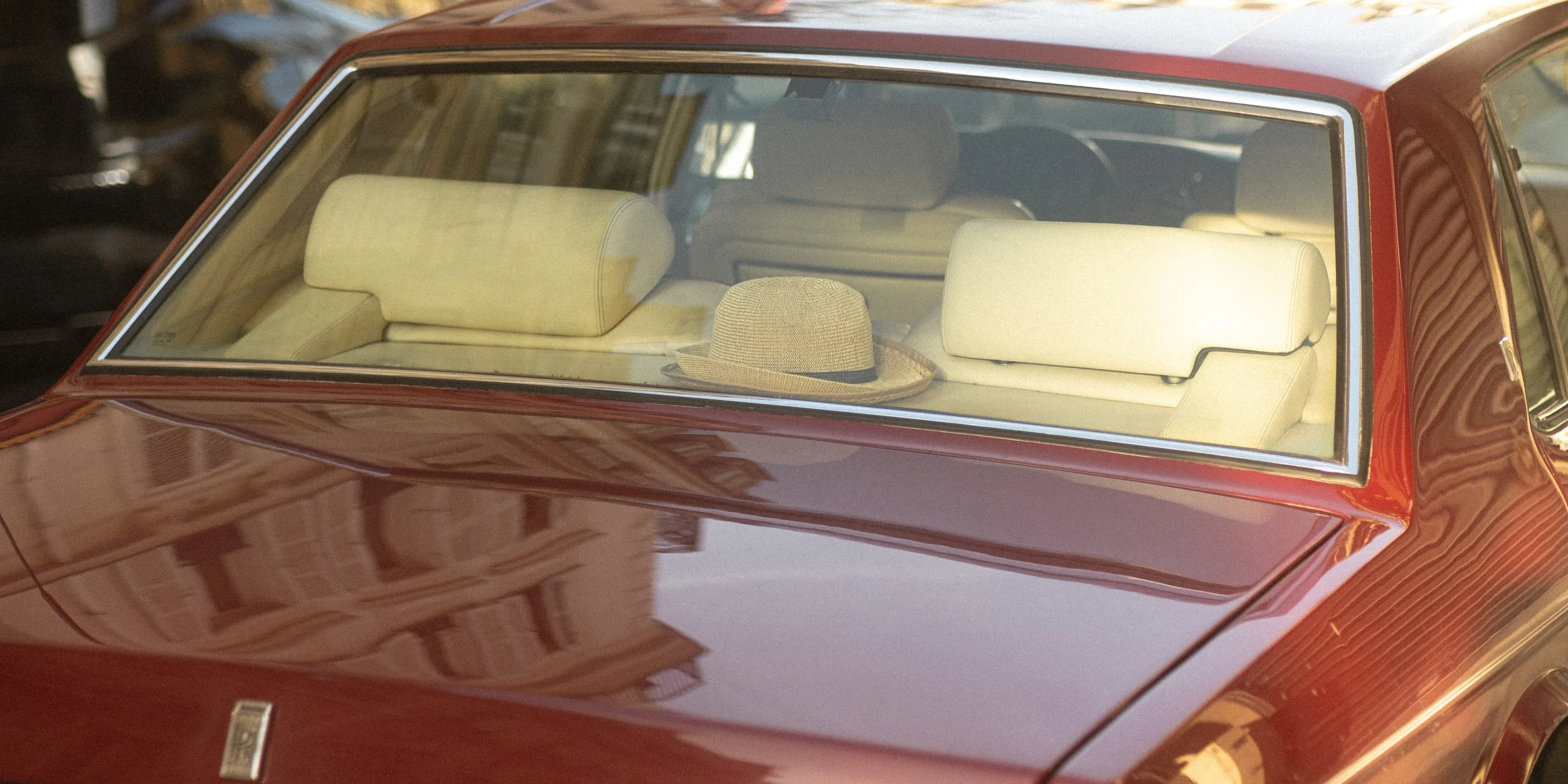 Front view of a vintage red car with a beige interior, showing a beige hat resting on the back seat through the windshield.