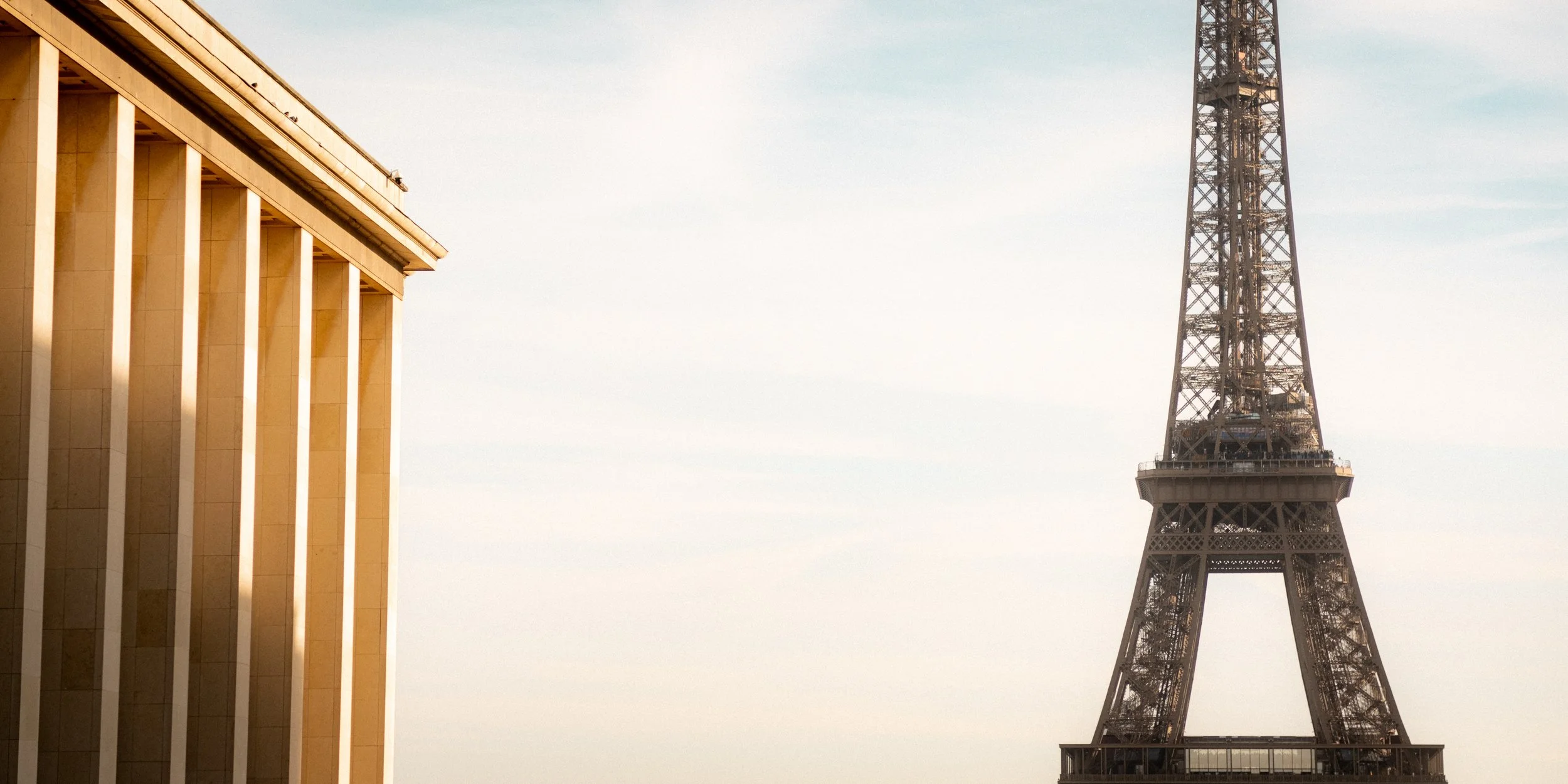 The Eiffel Tower in Paris with a portion of a building with tall columns on the left.