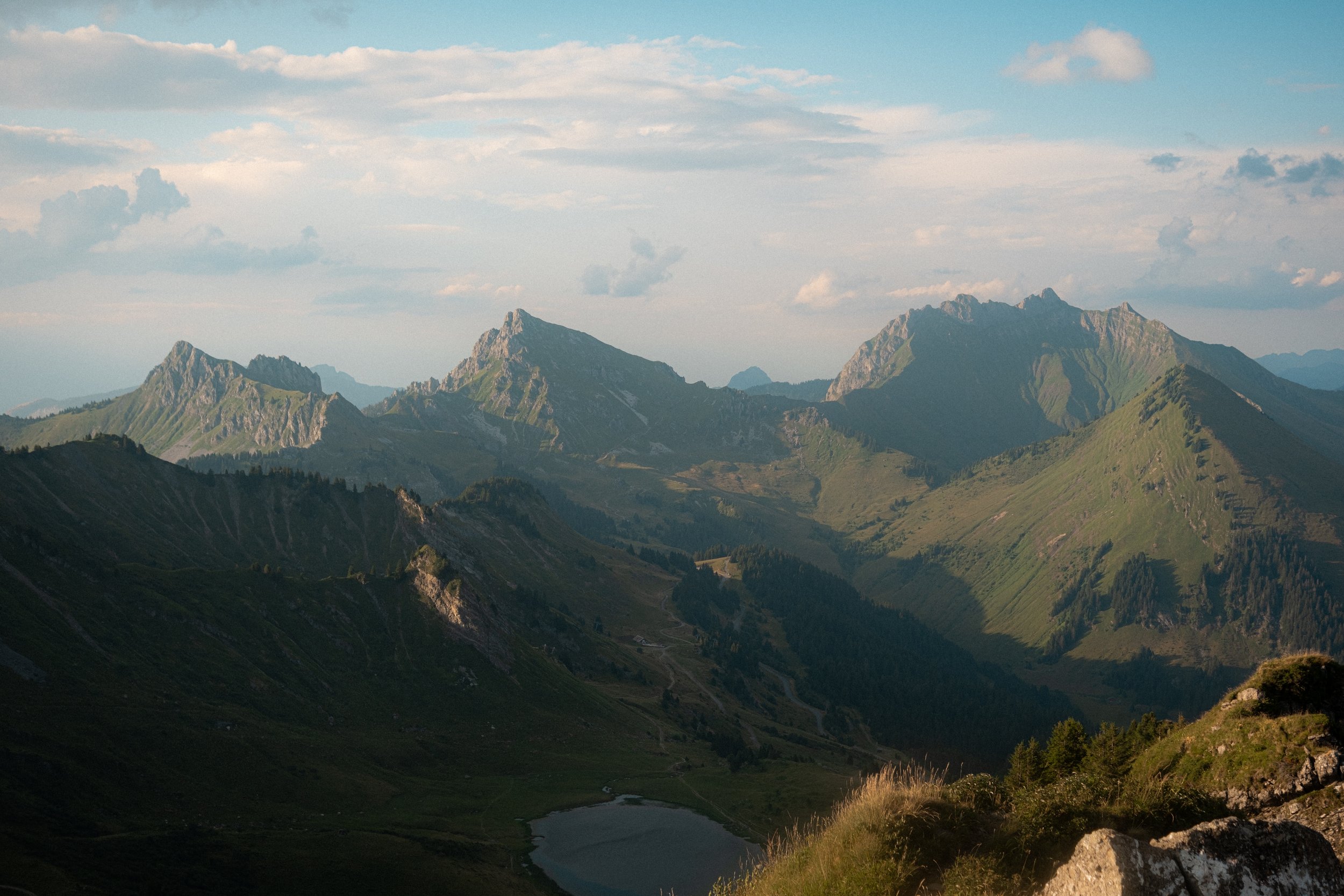 Scenic view of green mountains, a river flowing through a valley, with partly cloudy sky.