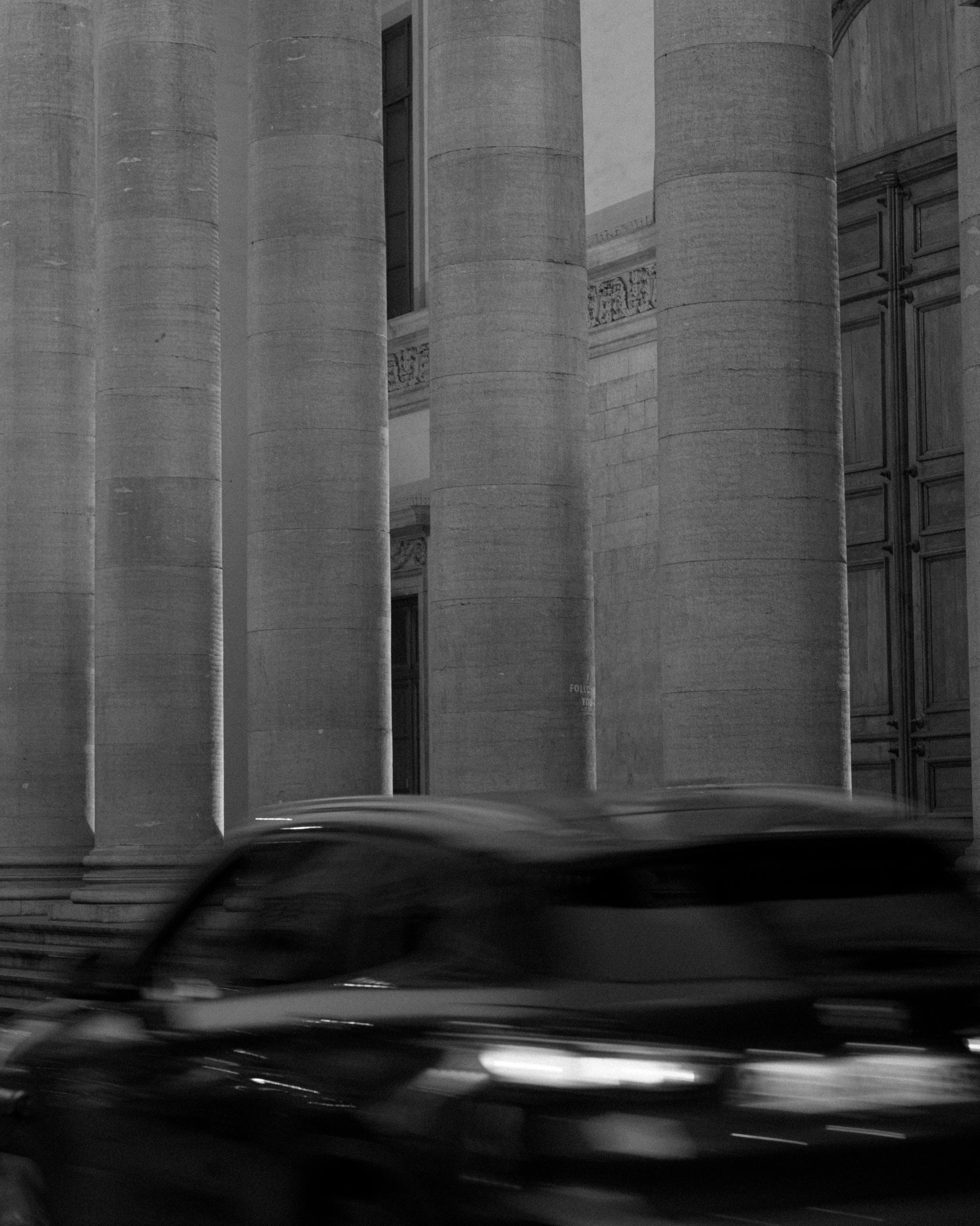 Black and white photo of large stone columns of a historic building with a partially visible ornate frieze and a closed door to the right.
