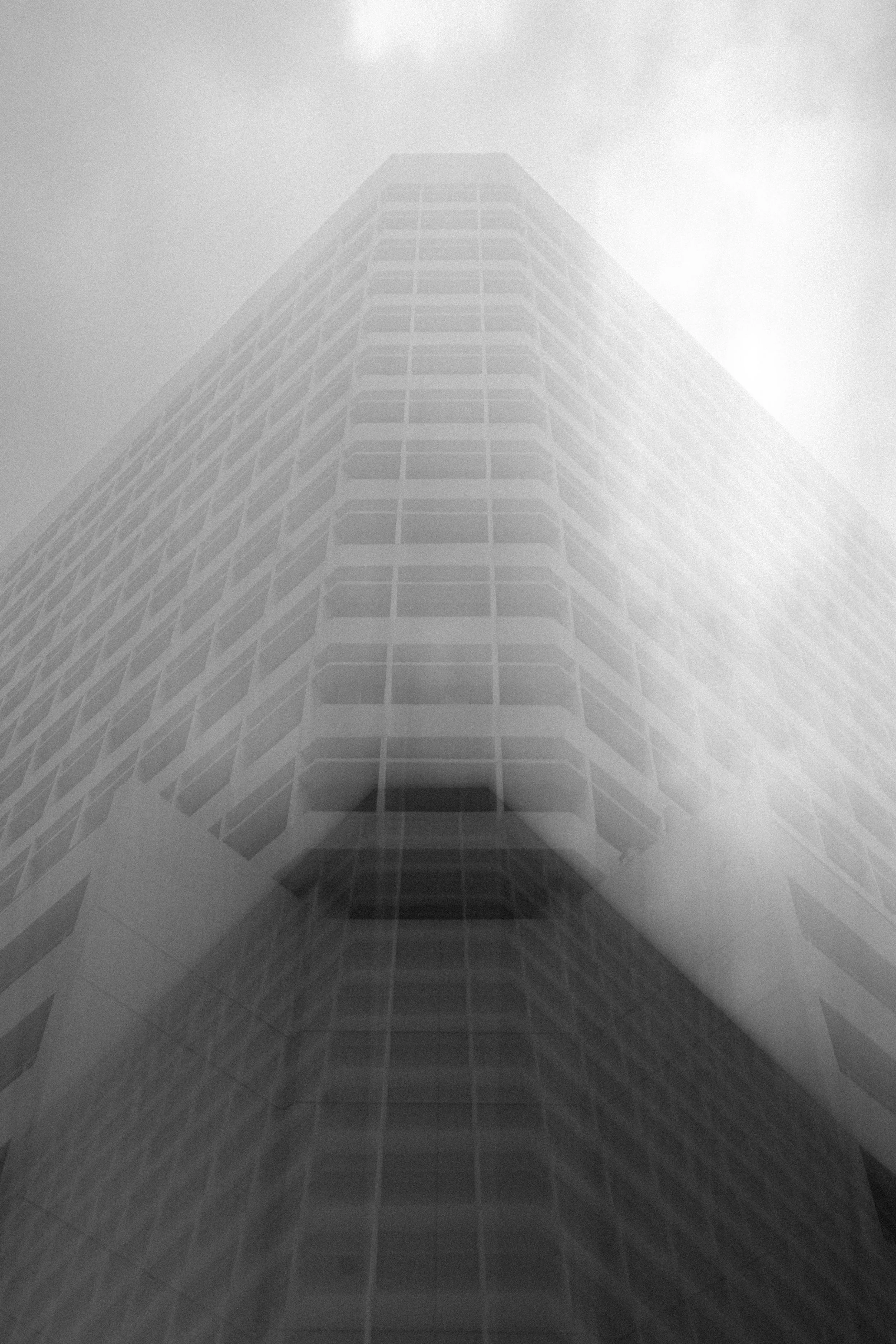 A tall modern building with a grid-like pattern of windows on its facade, partially obscured by fog or low clouds.
