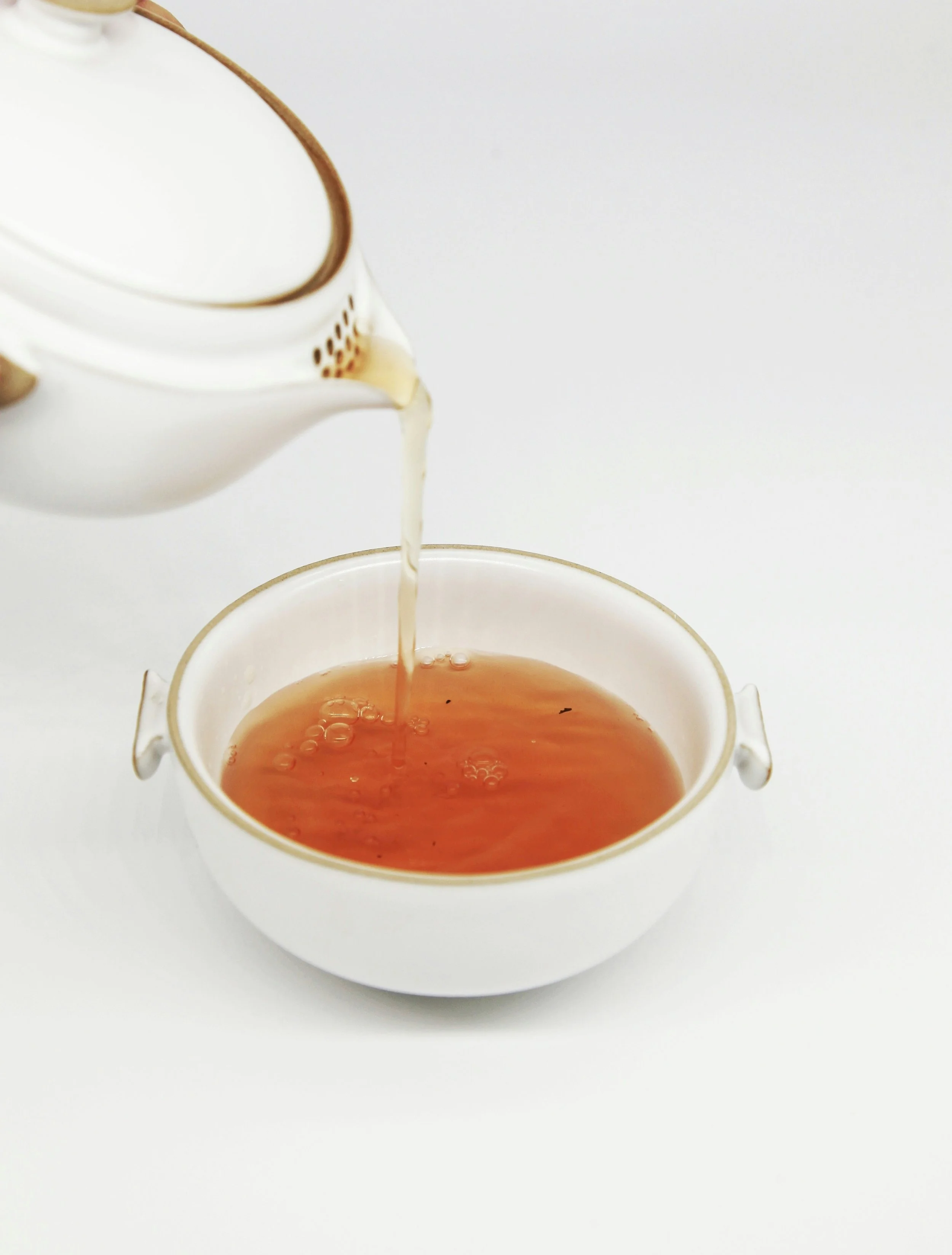Cream being poured from a teapot into a cup of tea.