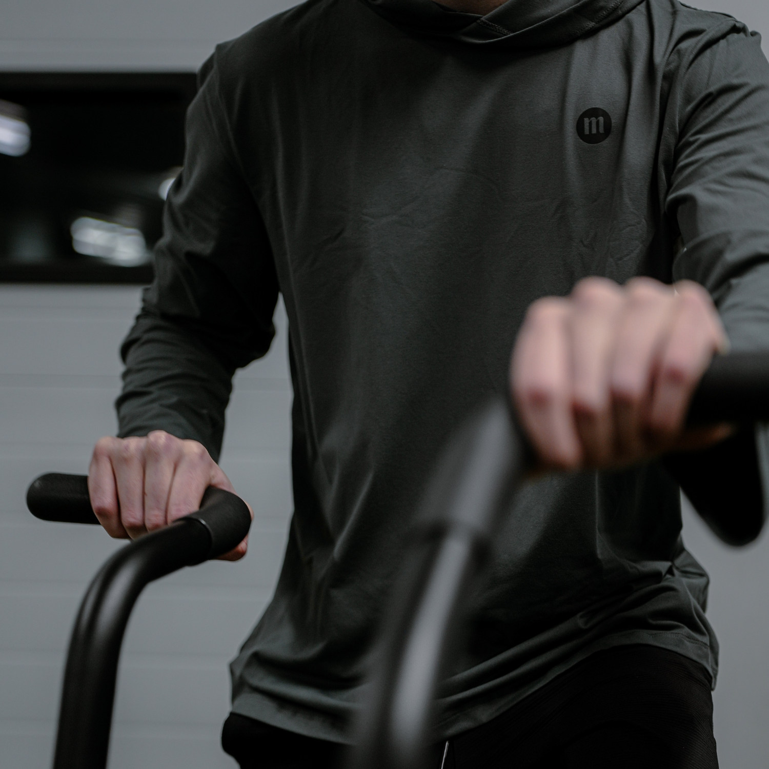 Person in black hoodie riding a stationary bike in a gym.