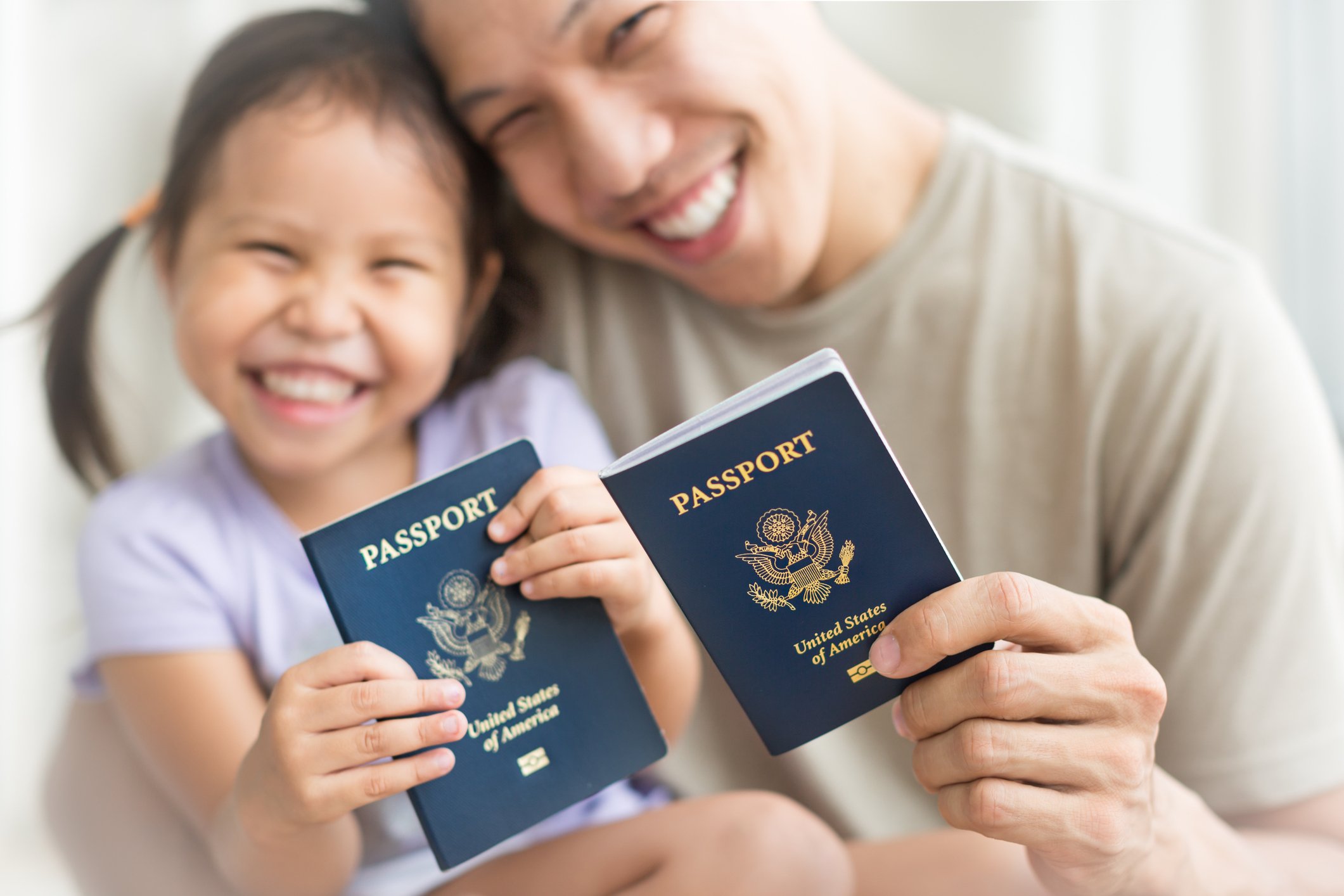 A smiling adult man and young girl holding U.S. passports, close together, with happy expressions.