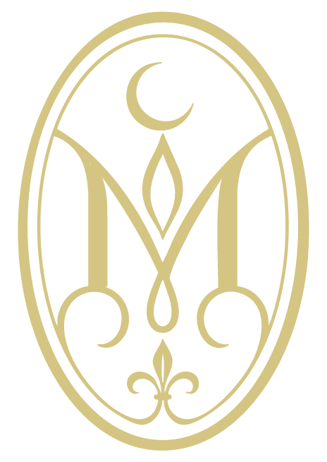 A black and gold logo featuring a crescent moon at the top, ornate design, and a stylized letter M in the center, enclosed in an oval outline.