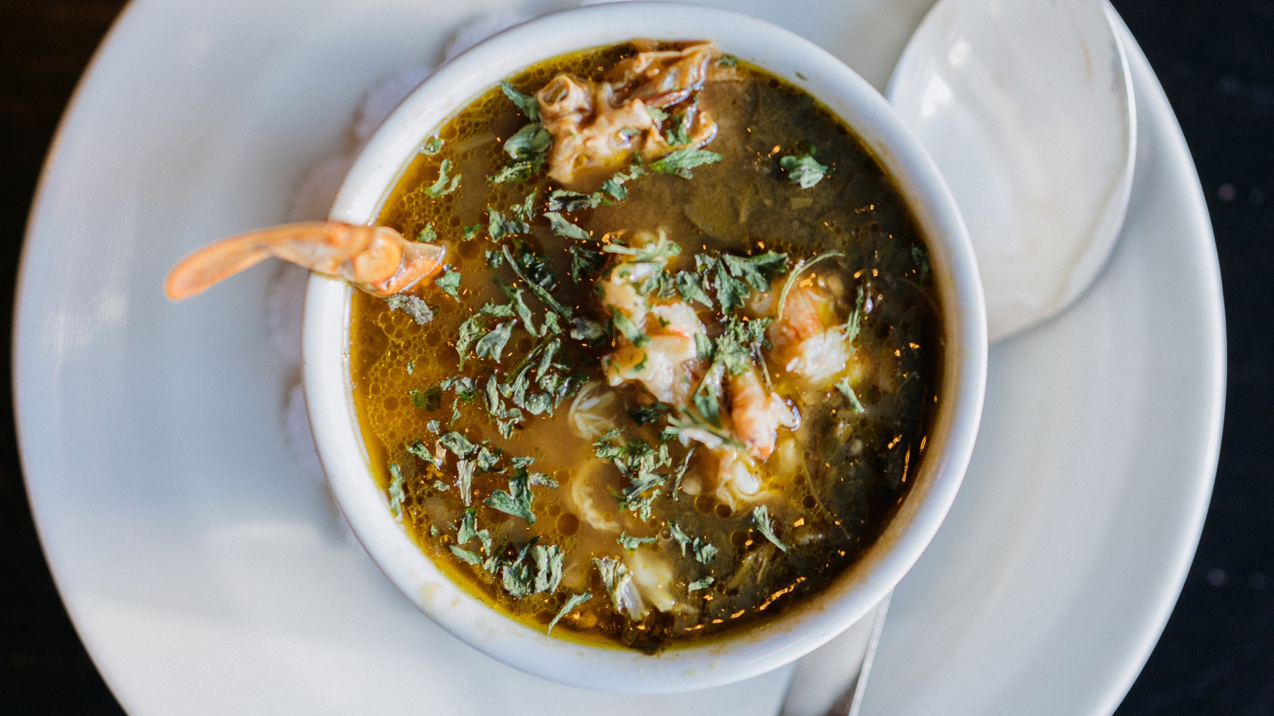 A bowl of seafood soup garnished with chopped herbs on a white plate.