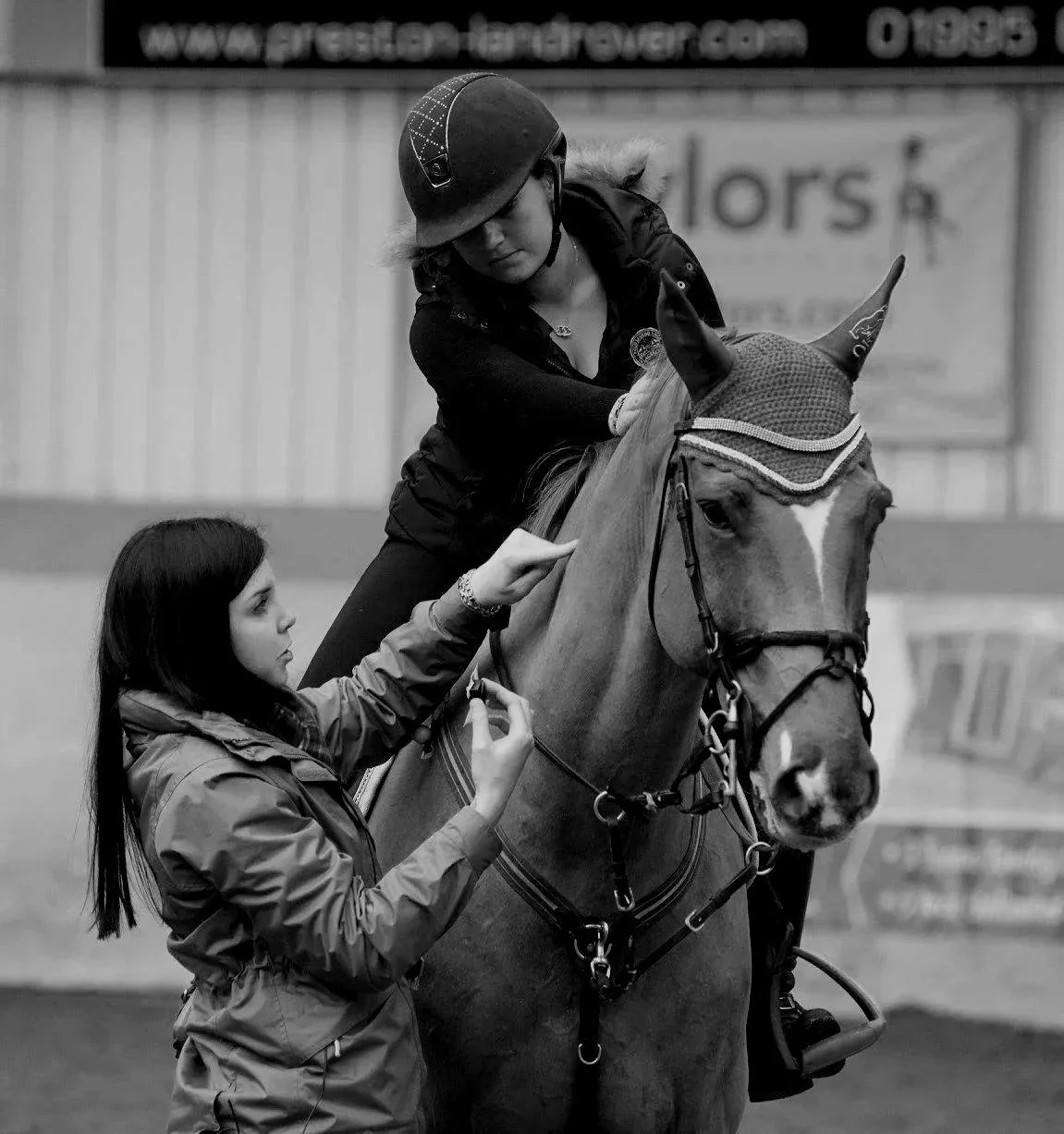 A woman explains how to attach surface electromyography sensors to a horse. The horse has a rider and is wearing a stitched ear bonnet.