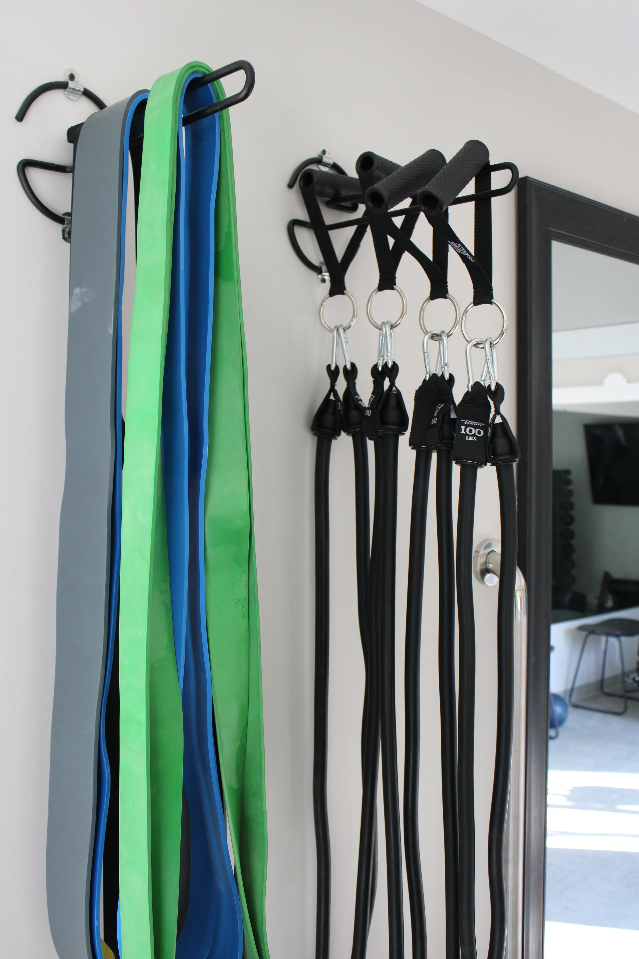 Resistance bands in various colors and exercise straps hanging on hooks inside a gym or fitness room.