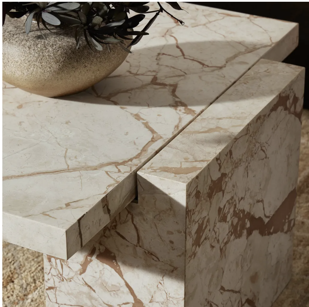 Close-up of a marble side table with a golden plant pot and green plant on top.