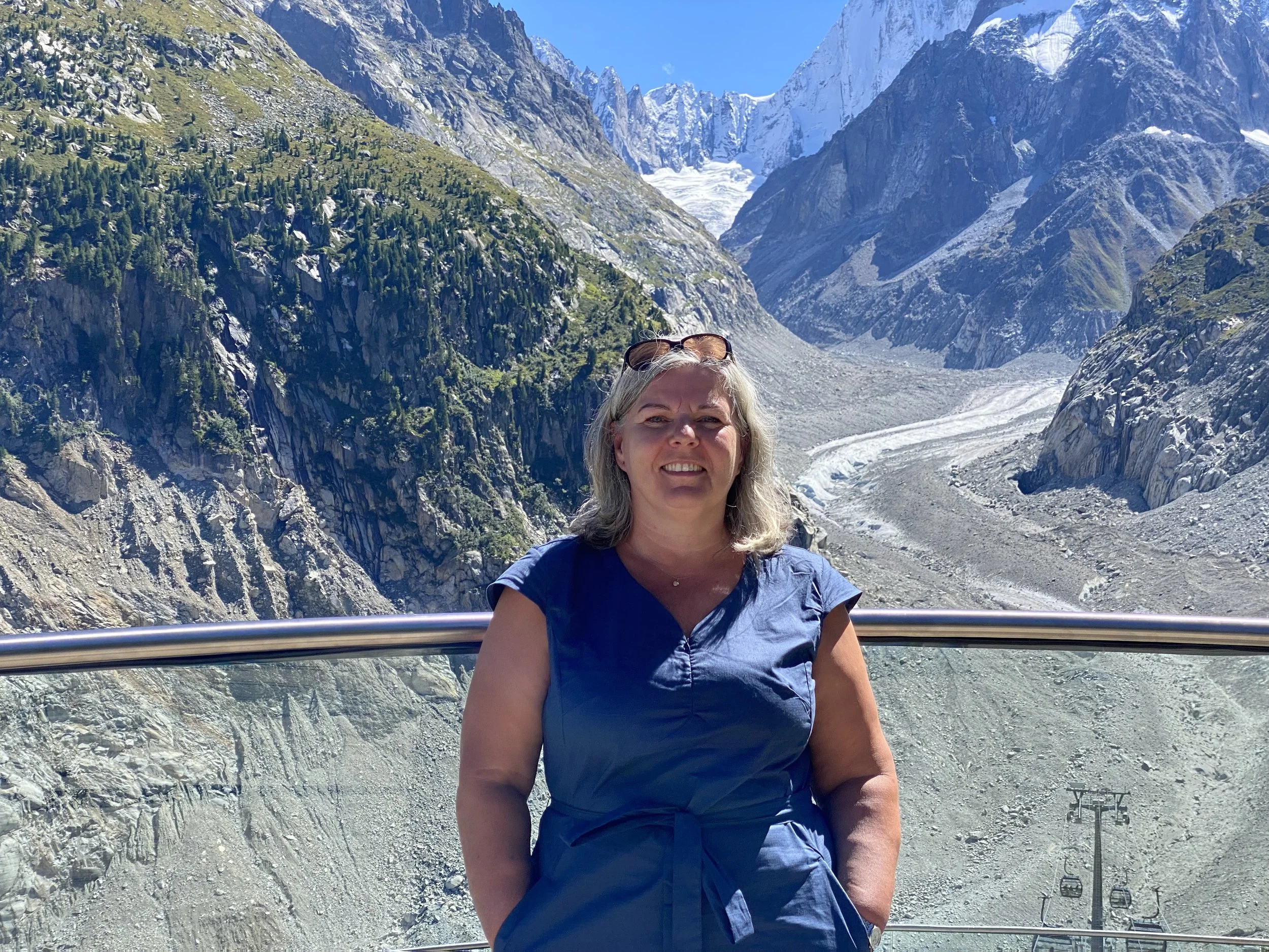 A woman standing on a mountain viewing platform with snowy mountains and glaciers in the background.