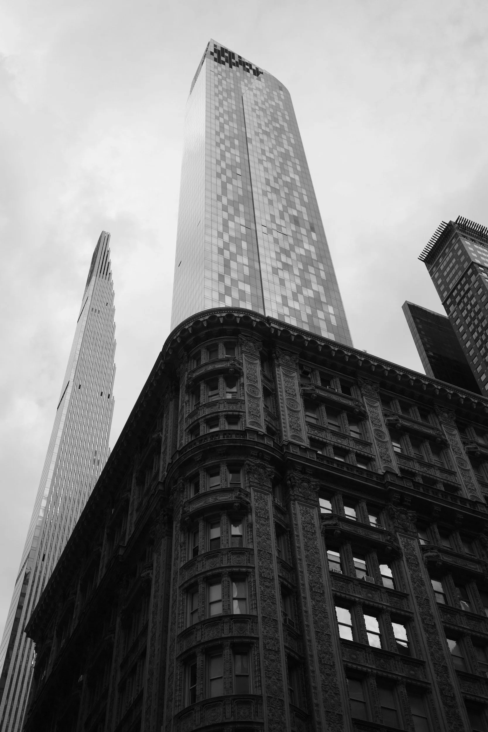 Black and white photo of skyscrapers in a city, featuring a historic ornate building at the bottom and a modern glass tower reaching skyward.