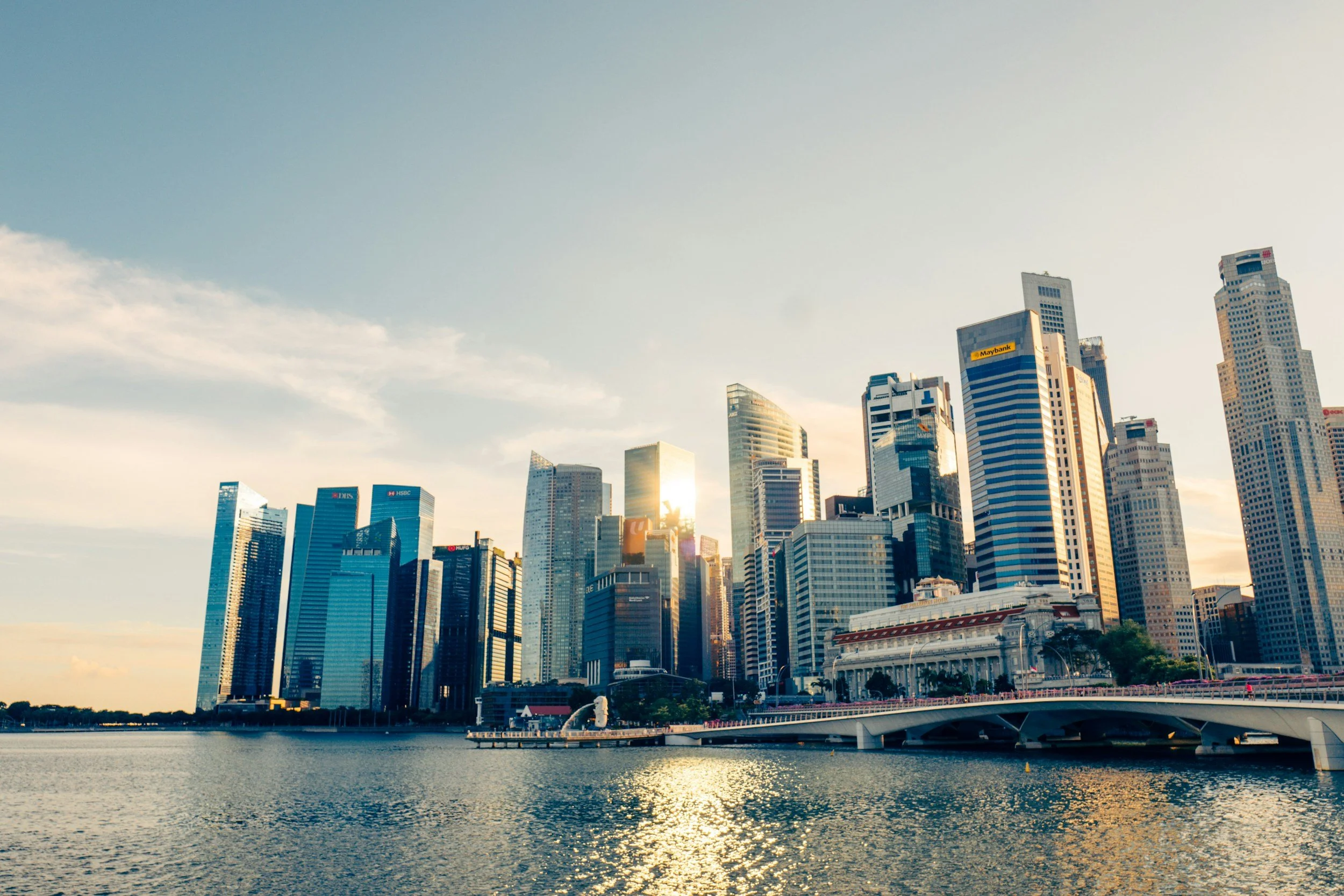 City skyline of skyscrapers and tall buildings along a water body during sunset with a bridge in foreground.
