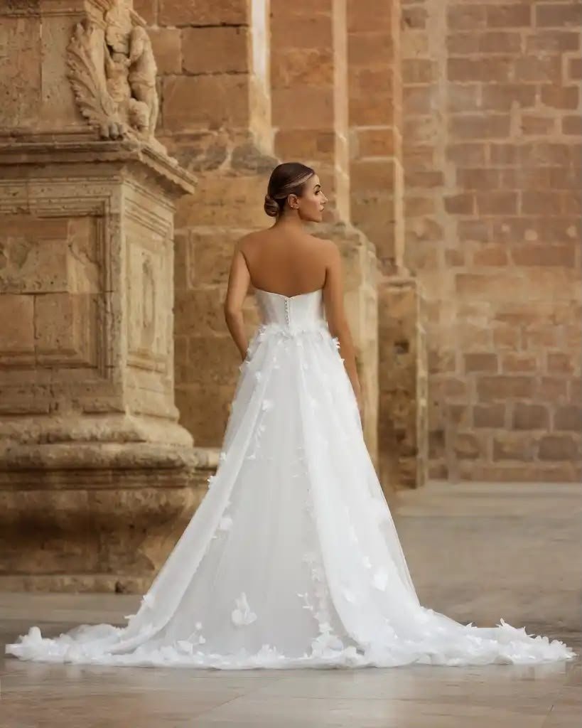 Bride in a strapless white wedding gown with a long train standing in a historic stone hall