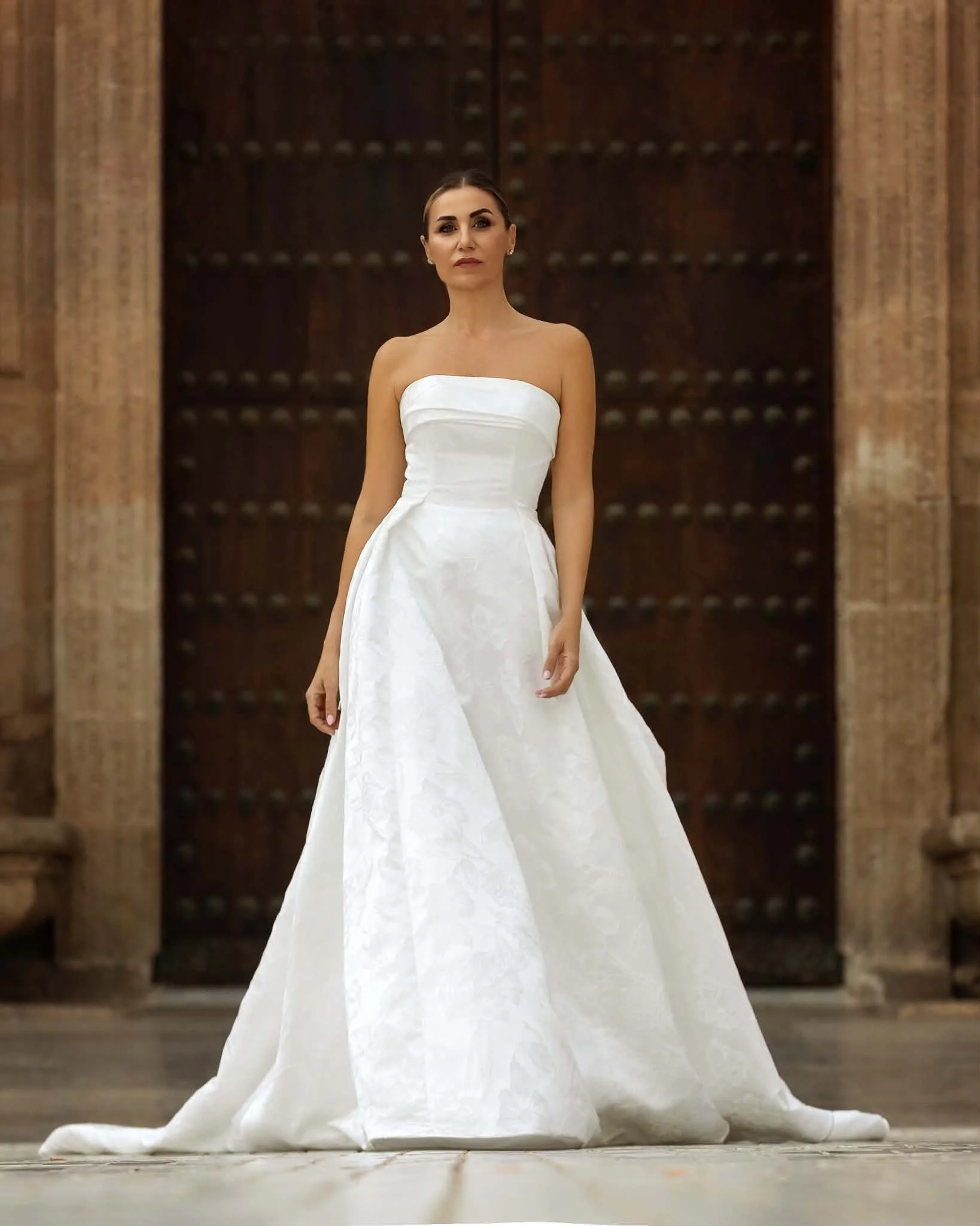 Woman modeling a strapless white wedding gown in front of a historic wooden doorway