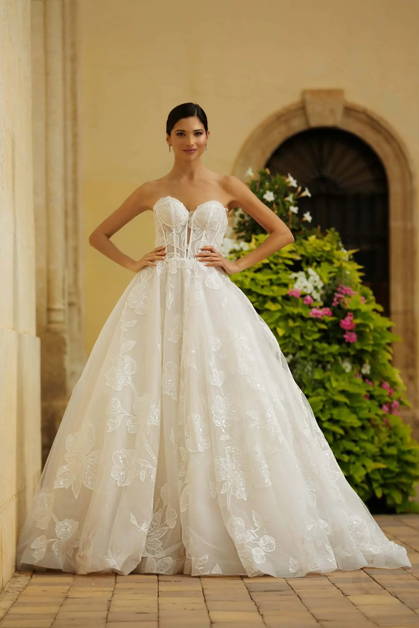 Bride modeling an embroidered strapless white wedding gown in a sunlit courtyard