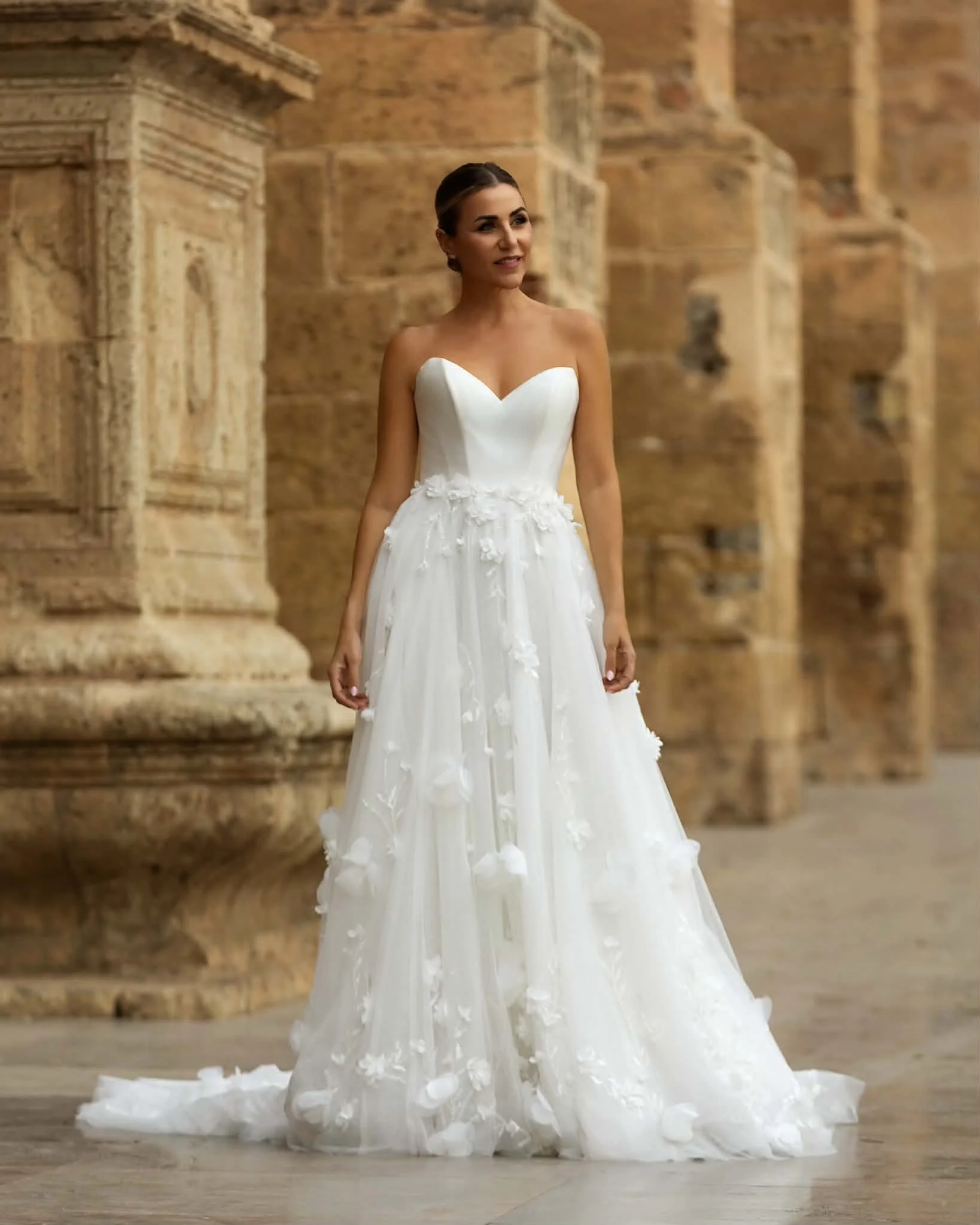 Bride in a white floral wedding gown standing among ancient stone ruins