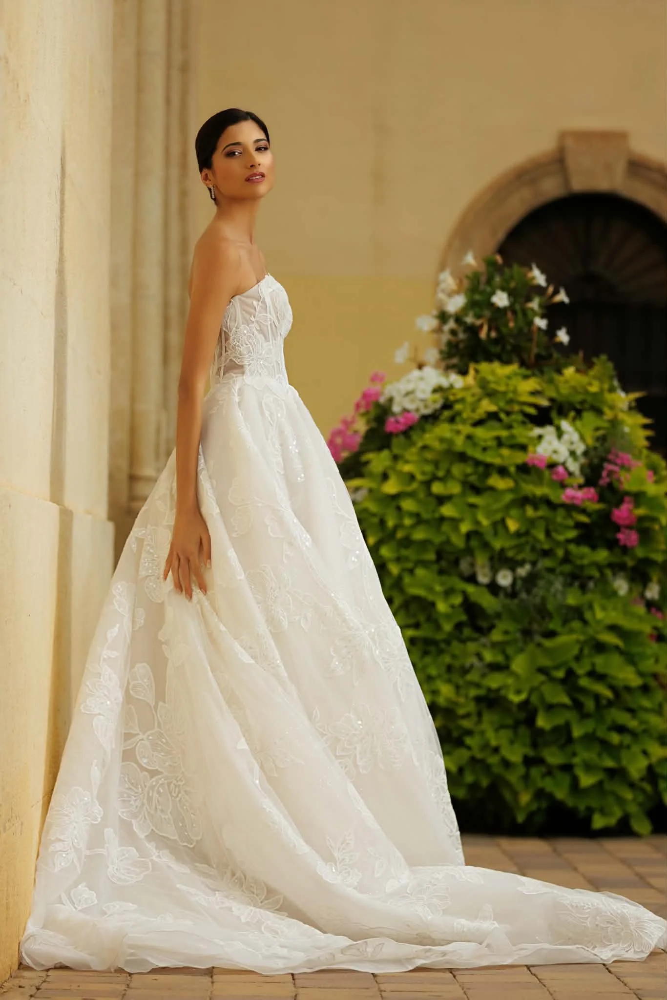 Woman modeling a strapless white floral lace wedding gown with a long train outdoors