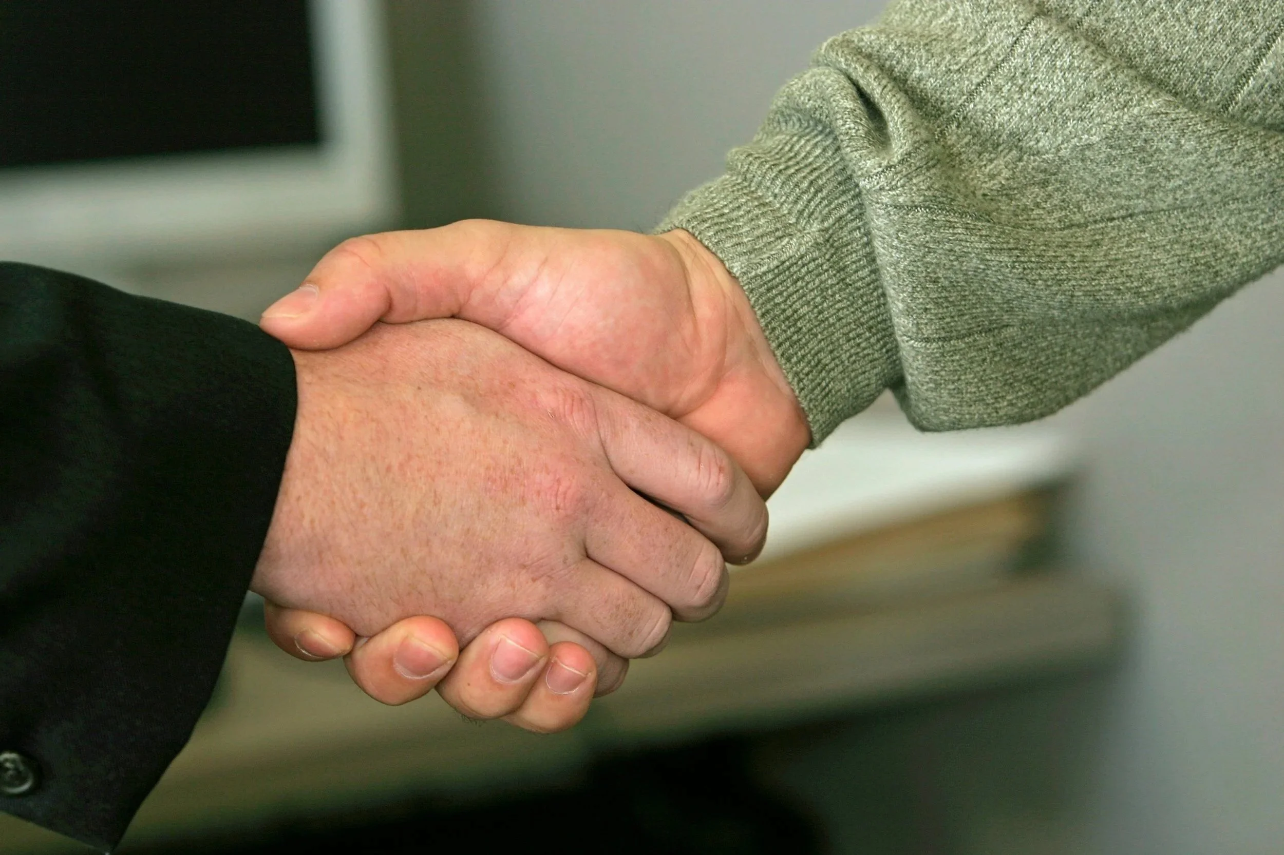 Two people shaking hands, one in a black suit and the other in a gray sweater.