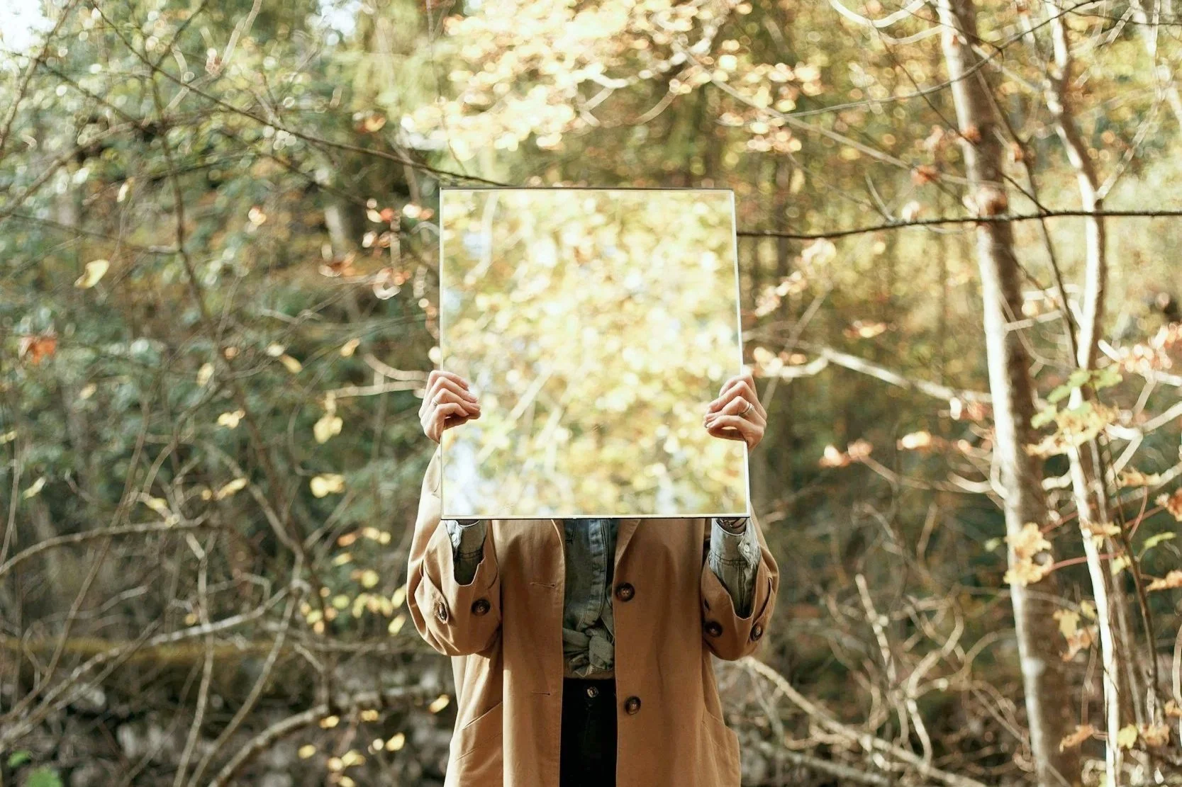 A woman holding a mirror in a forest.