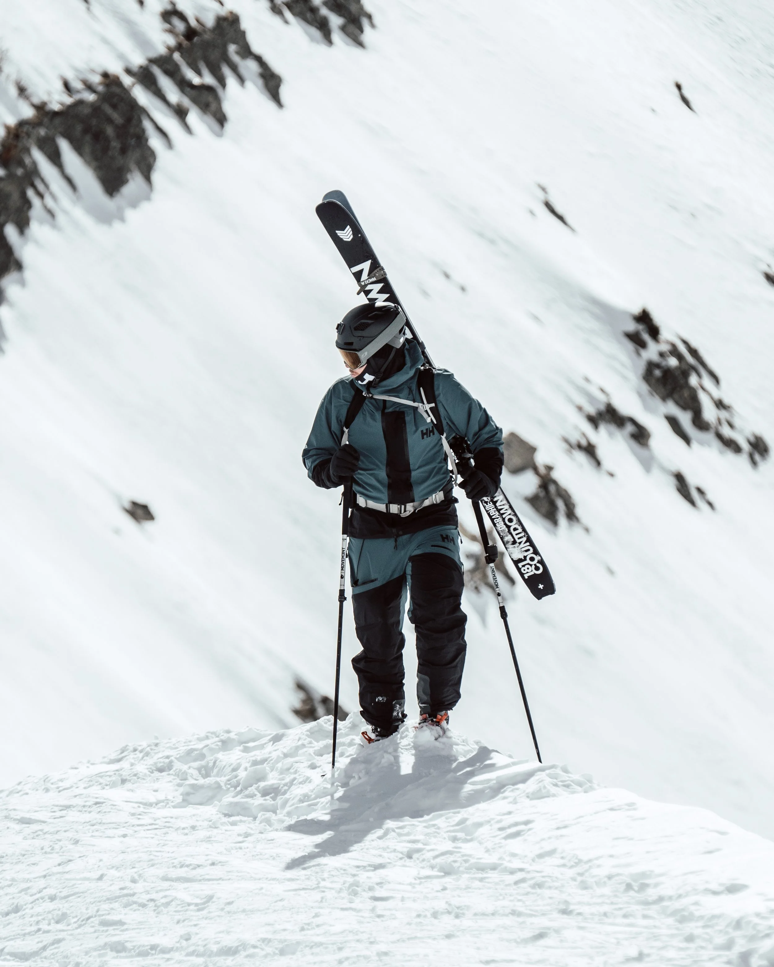 Personne en tenue de ski avec un casque et des skis, marchant dans la neige en montagne.