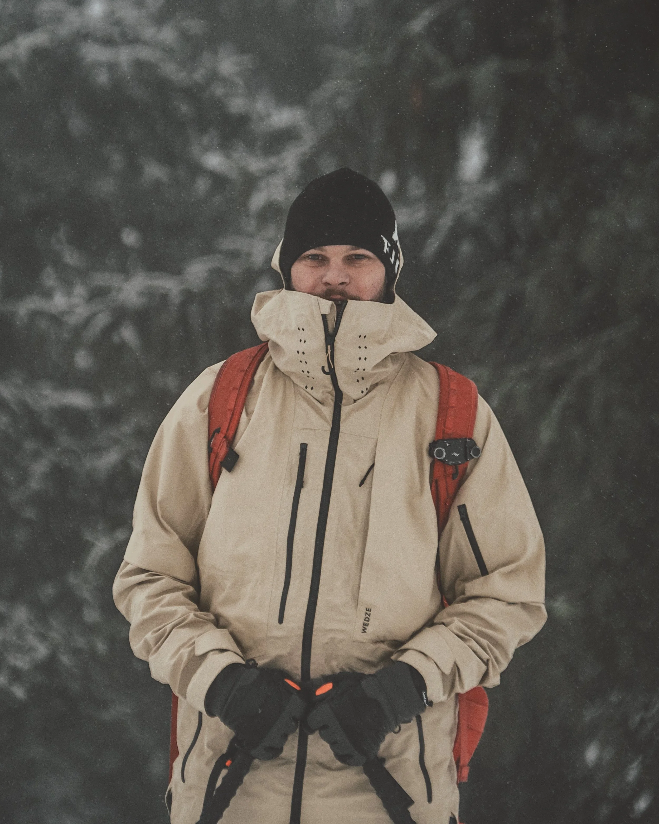 Un homme habillé en vêtements d'hiver, portant un sac à dos rouge, dans un environnement enneigé avec des arbres en arrière-plan.