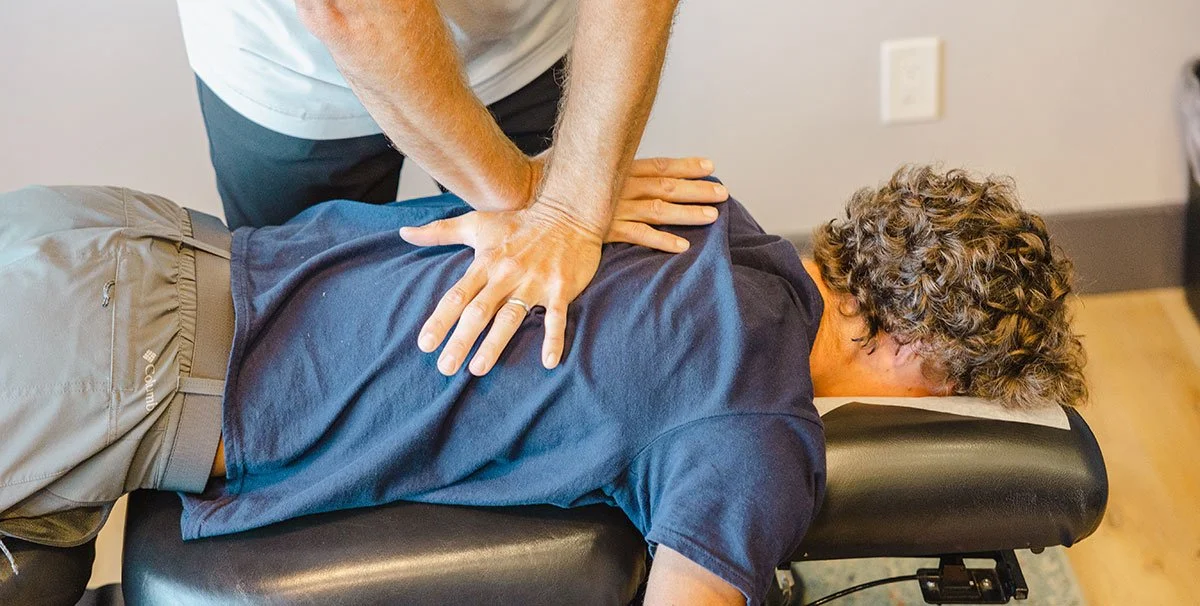 Chiropractor performing spinal adjustment on a patient lying face down on a chiropractic table.