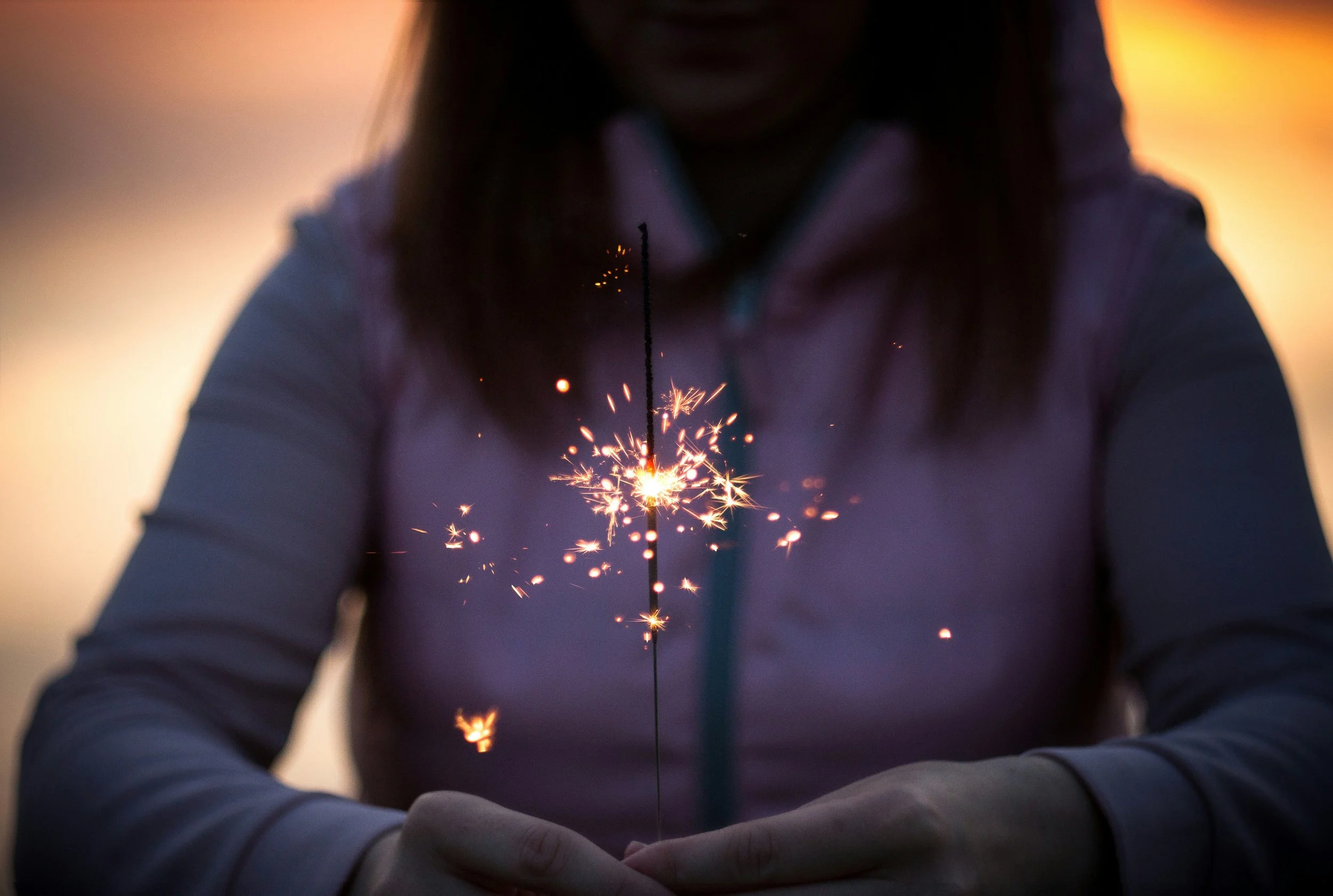 A child holding a lit sparkler during sunset to emphasize the "spark" portion of Spark Speech Therapy LLC.