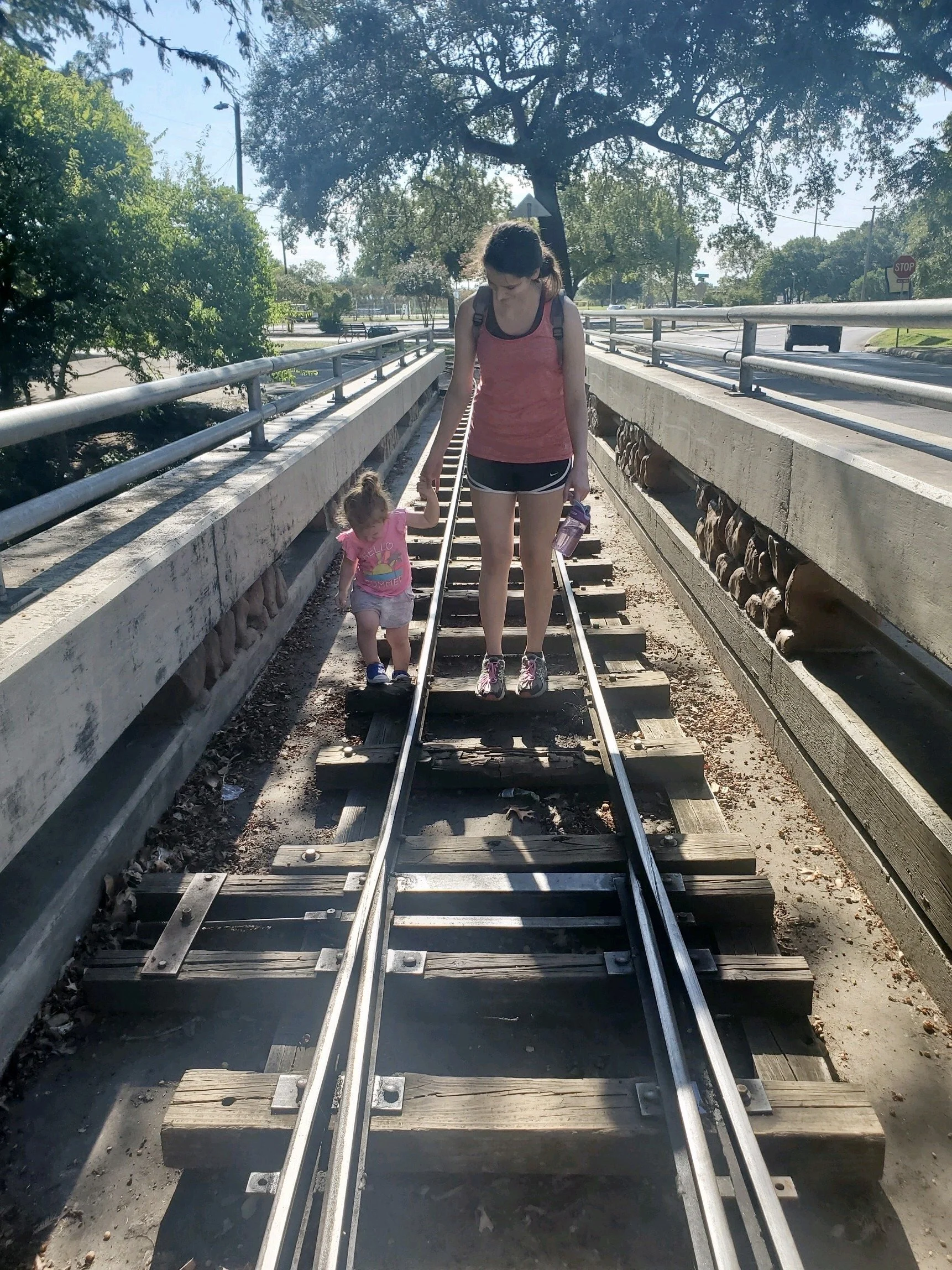 A woman holding hands with a toddler on railroad tracks.