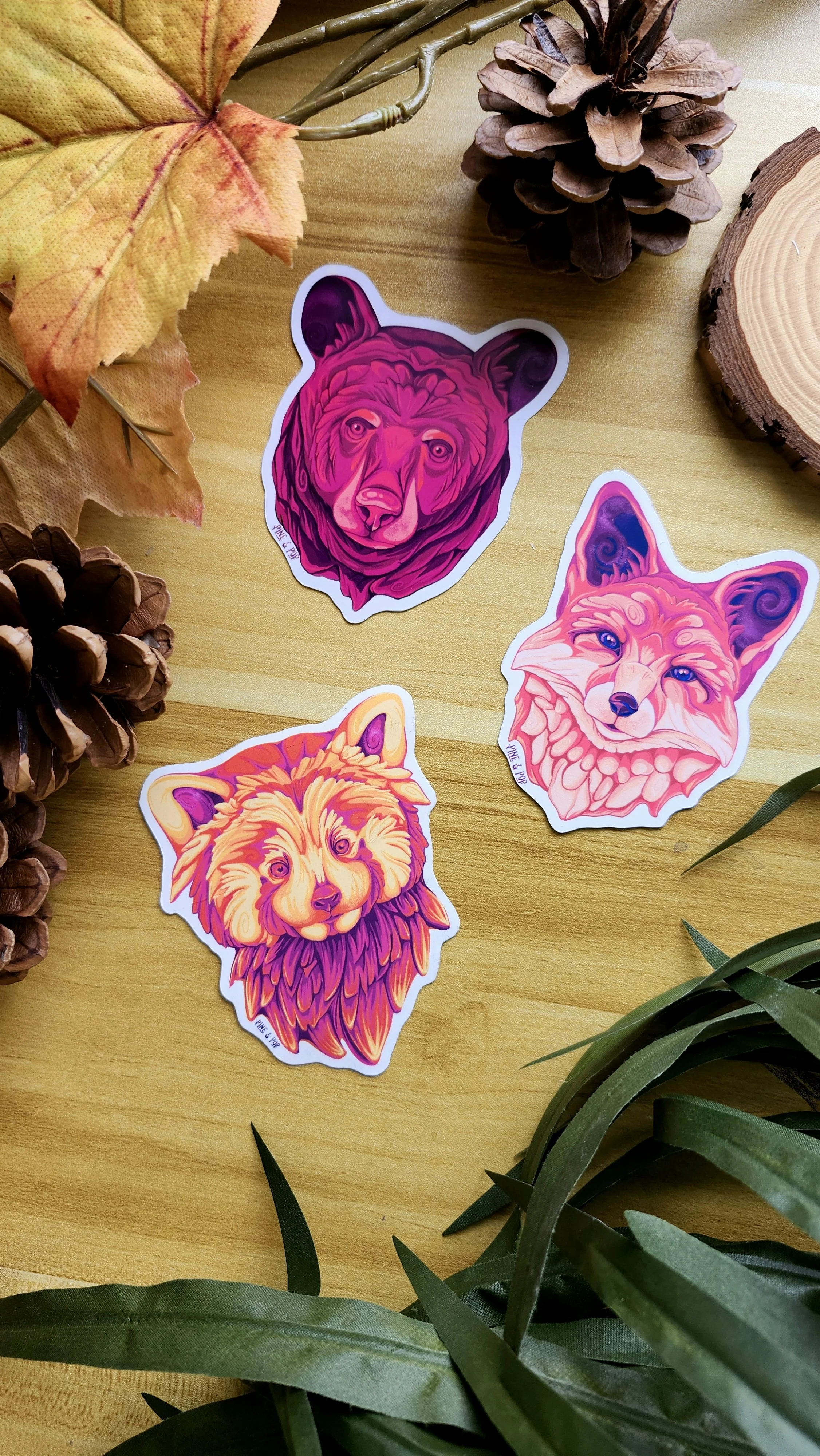 a red fox face magnet, a black bear face magnet, and a red panda magnet laying on a wooden table