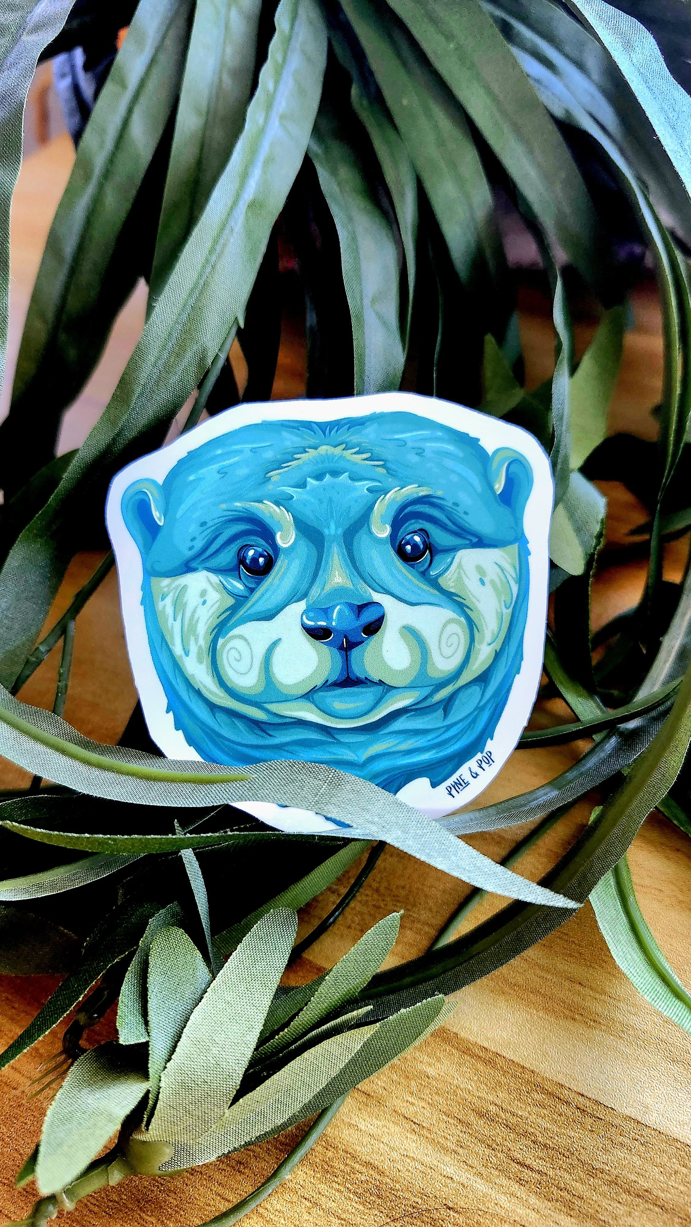 close up view of otter face sticker showing the details of the design and green, blue, and teal colors that make up the face