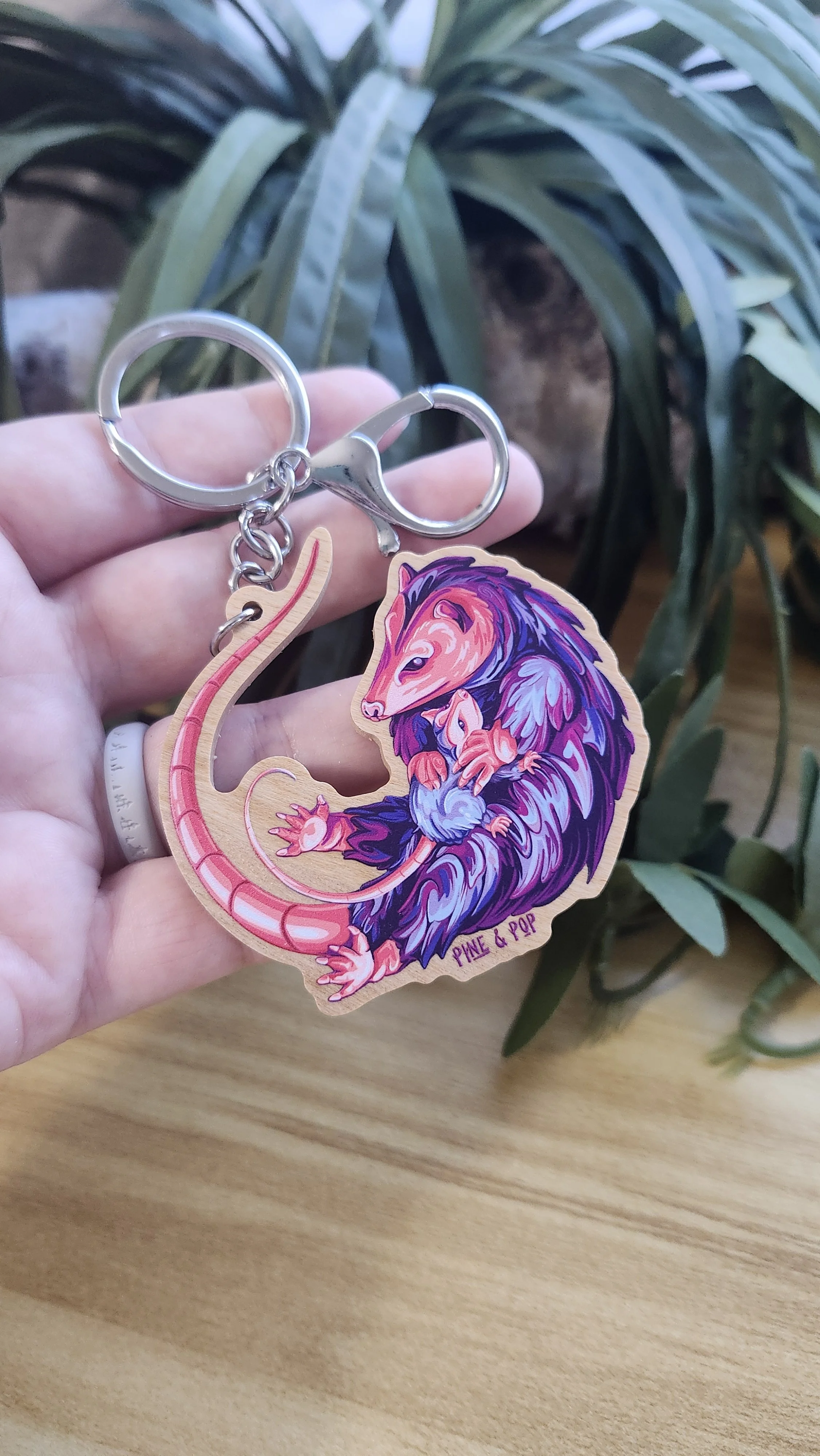 wooden keychain of opossum designed with bright blue, purple, pink, and coral colors
