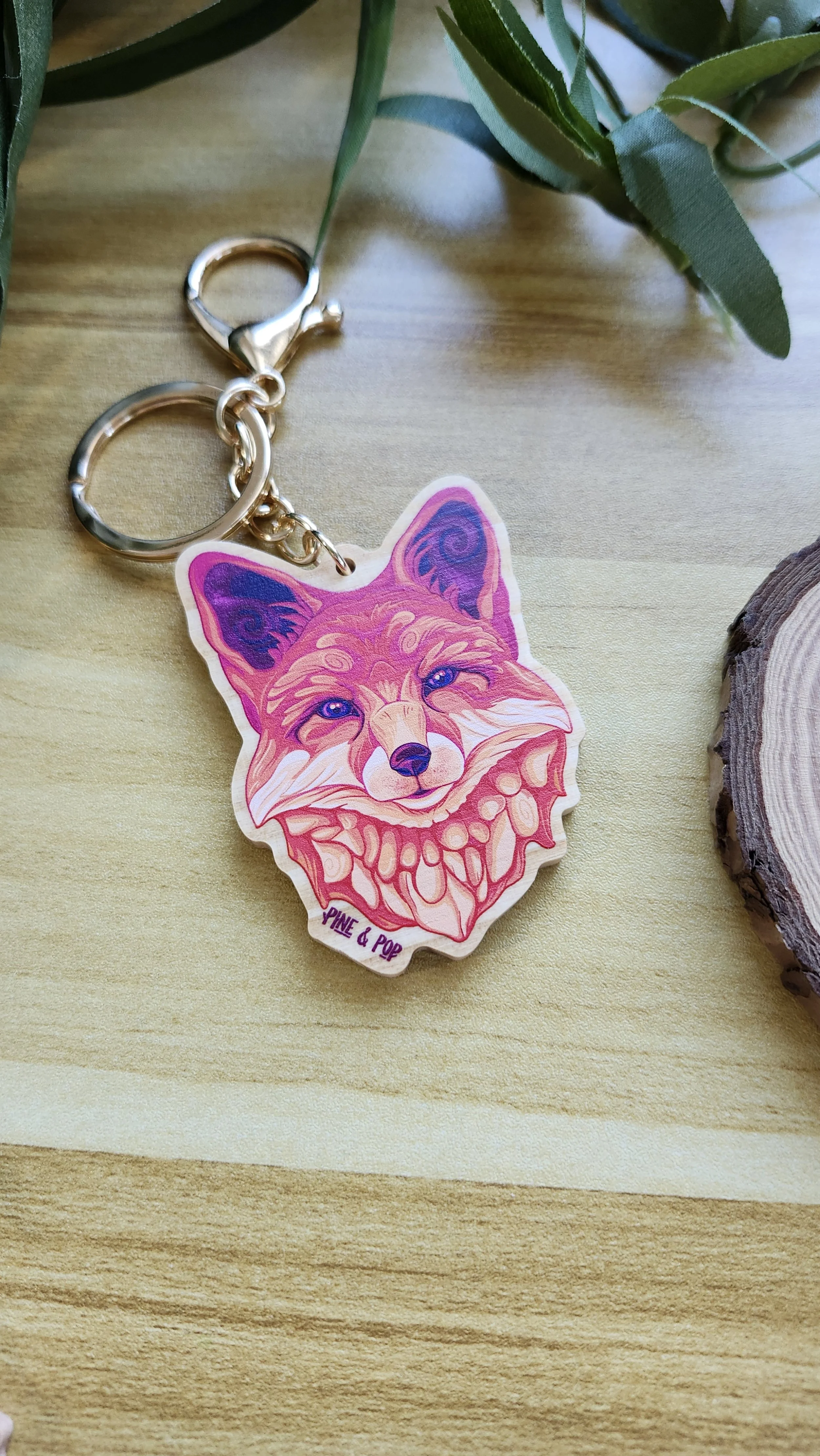 a keychain of a fox head with red, orange, cream, and purple colors used to create the design