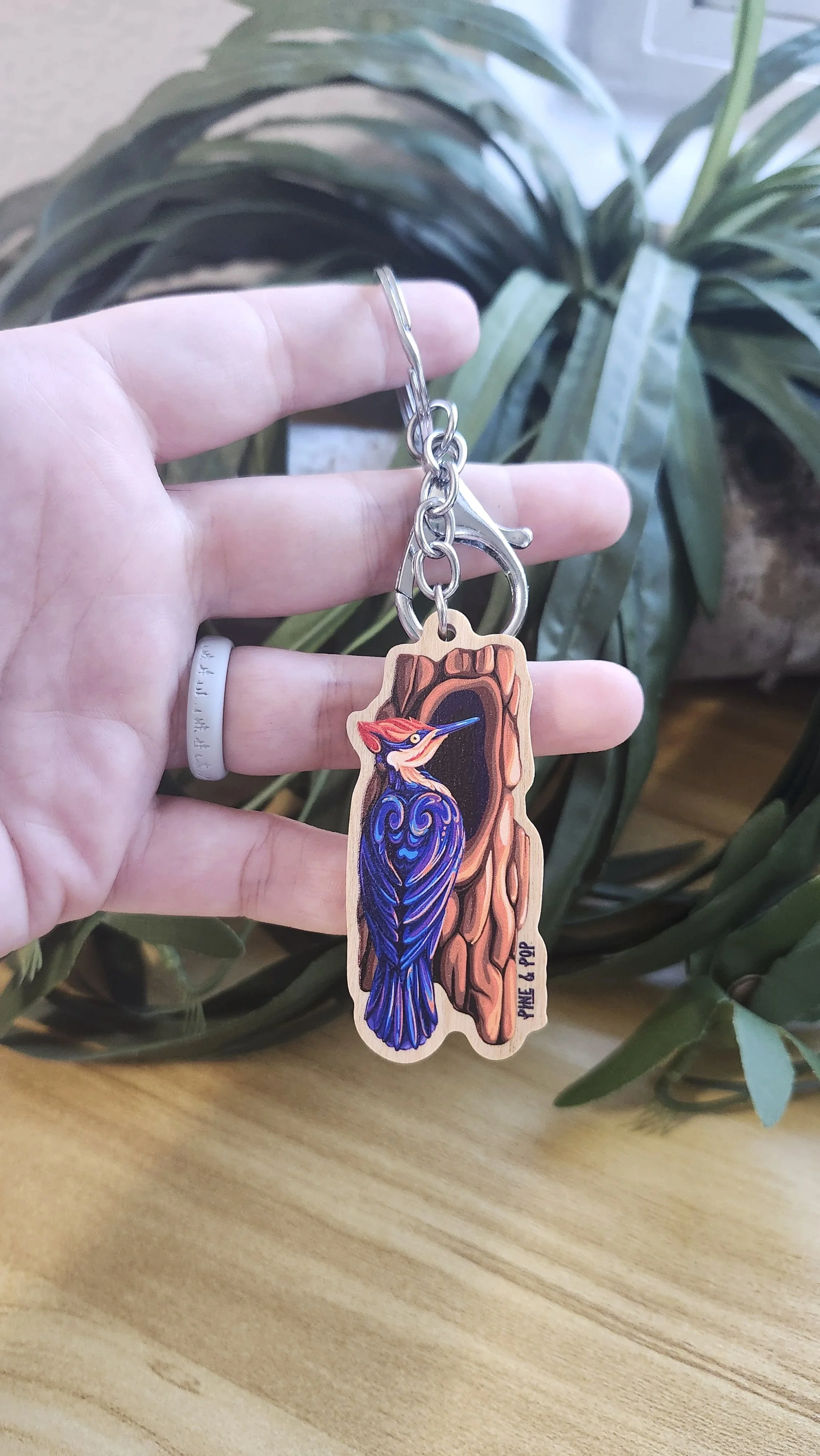 wooden keychain of pileated woodpecker next to tree hole made up of bold natural colors